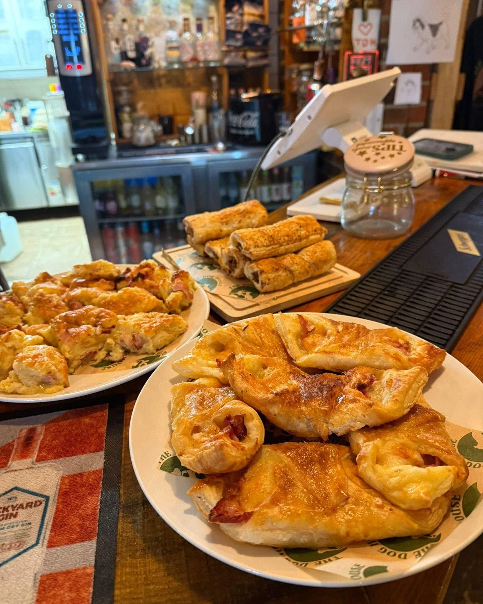 Pizza slices, rolled egg rolls, and chicken parmesan on plates on a bar counter inside a restaurant.