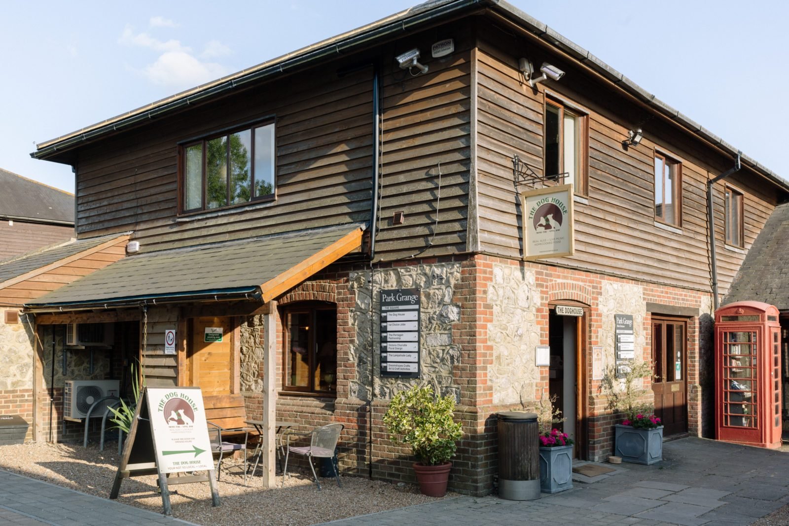 A two-story building with brick and wood exterior, sign for 'The Dog House', outdoor seating, and a red British telephone booth.