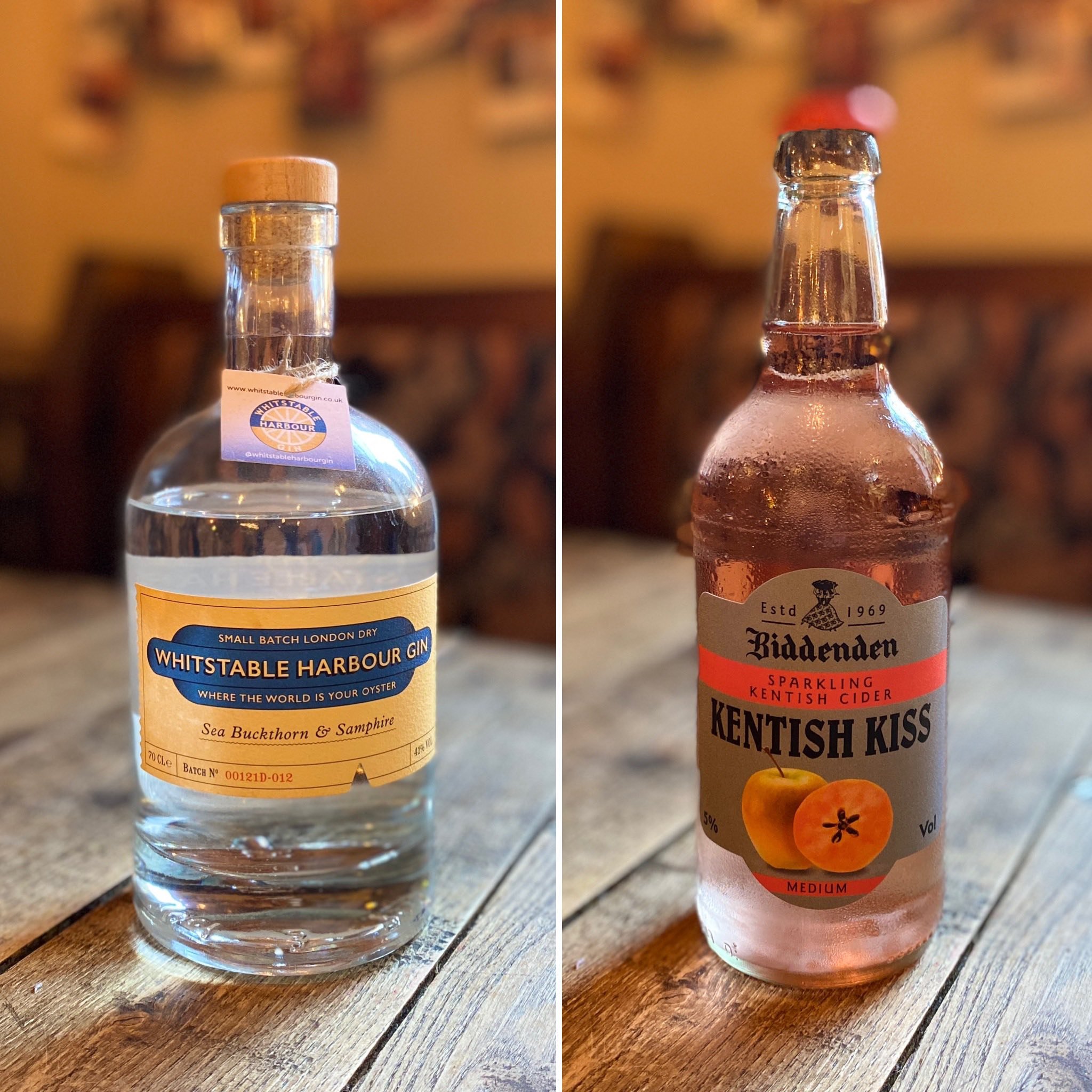 Two bottles on a wooden table: a bottle of Whitstable Harbour Gin on the left and a bottle of Biddenden Kentish Kiss sparkling cider on the right.