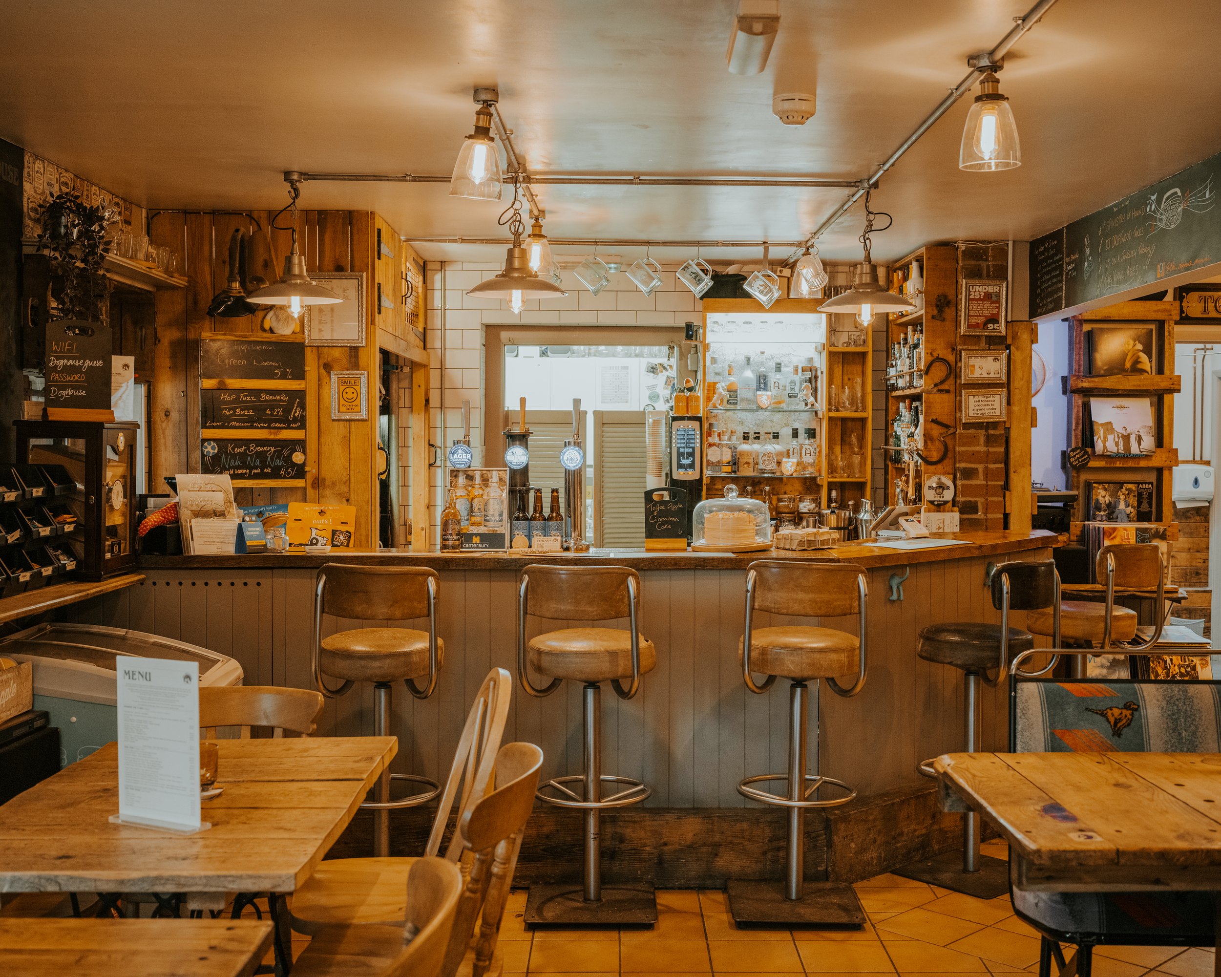 Interior of a cozy cafe with wooden furniture, bar stools at the counter, and warm lighting.