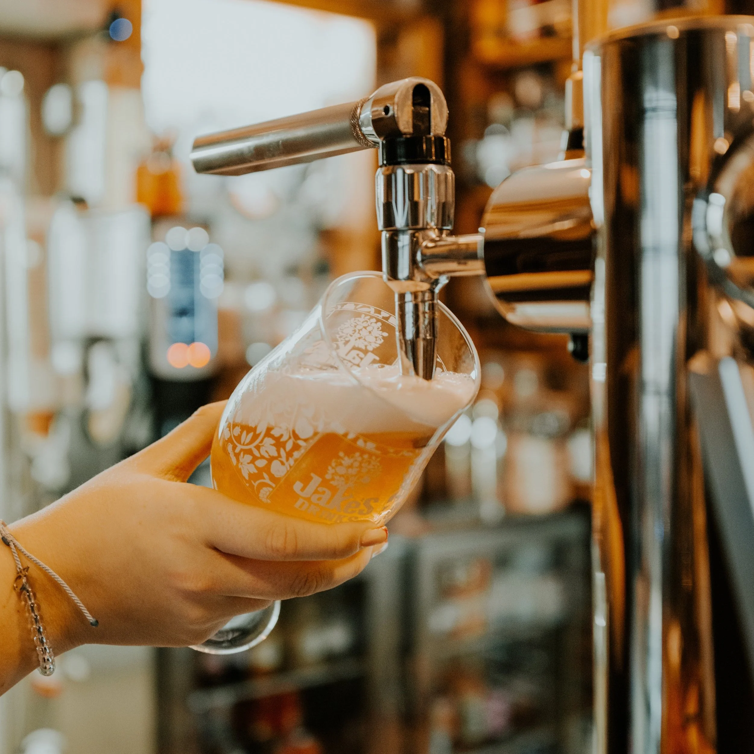 A person is pouring beer from a tap into a branded glass at a bar or brewery.