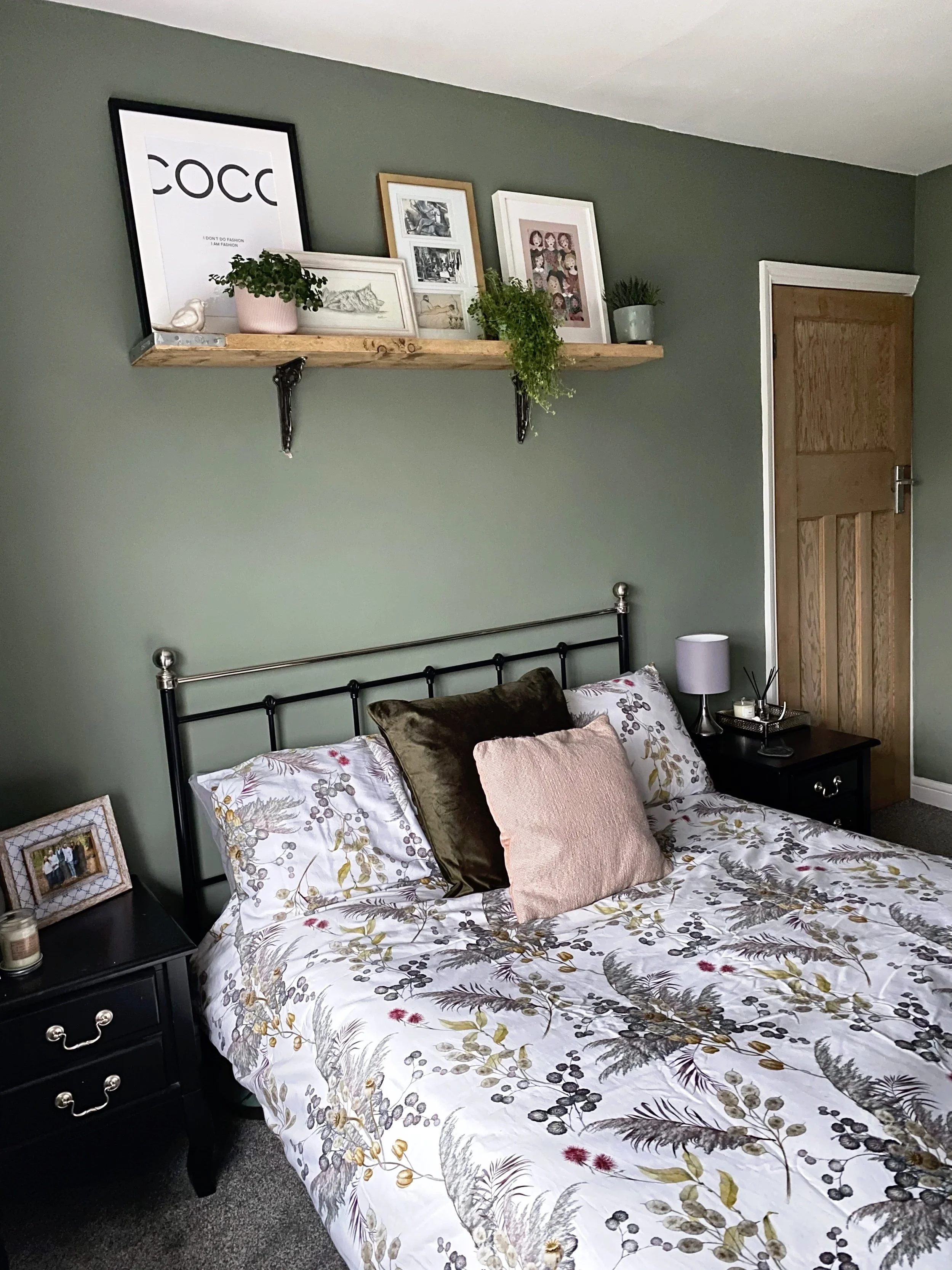 Green bedroom, a double bed, with floral bedding, bedside tables and a shelf on the wall holding multiple picture frames