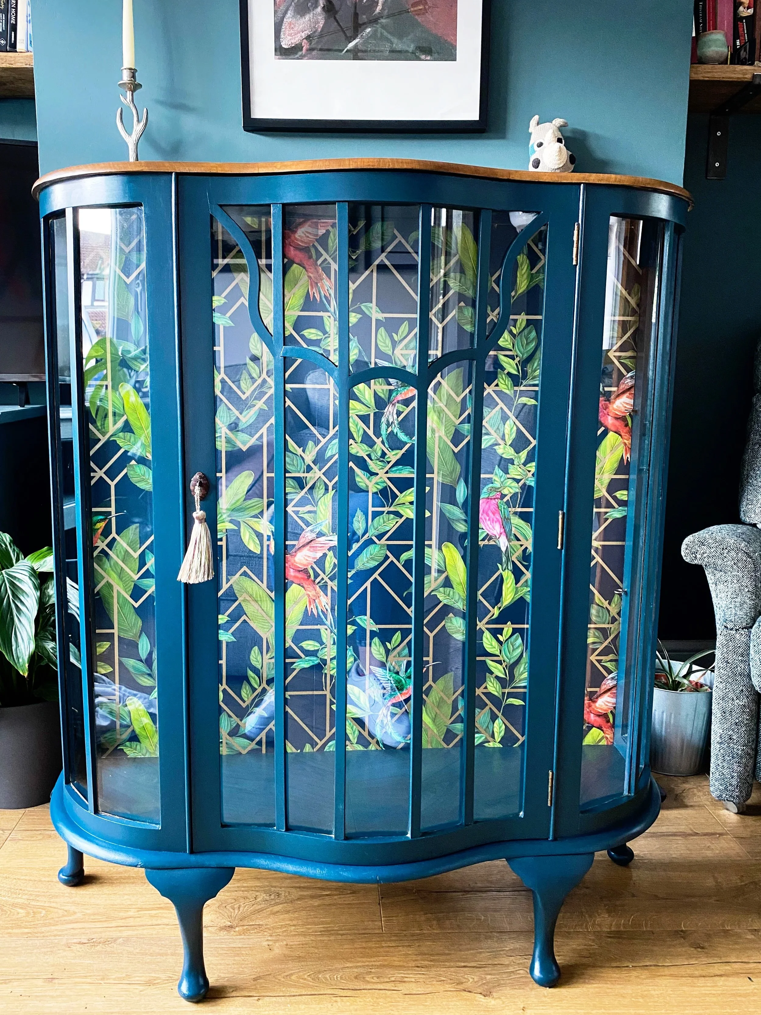 A traditional cabinet upcycled with blue paint and a vibrant wallpaper with tropical birds on it