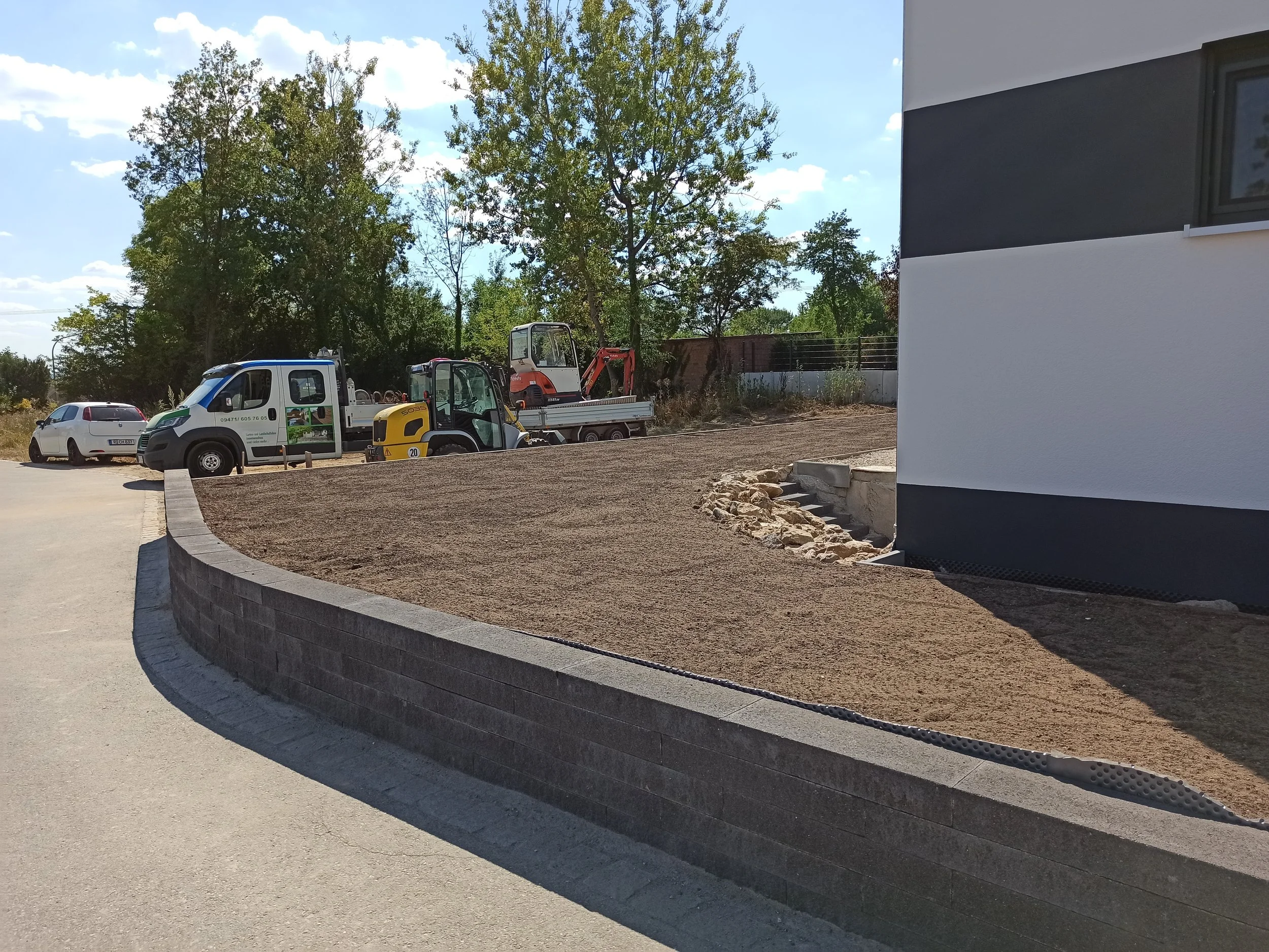 Baustelle mit Erdarbeiten, Baufahrzeuge und Parkplätze neben einem modernen Gebäude