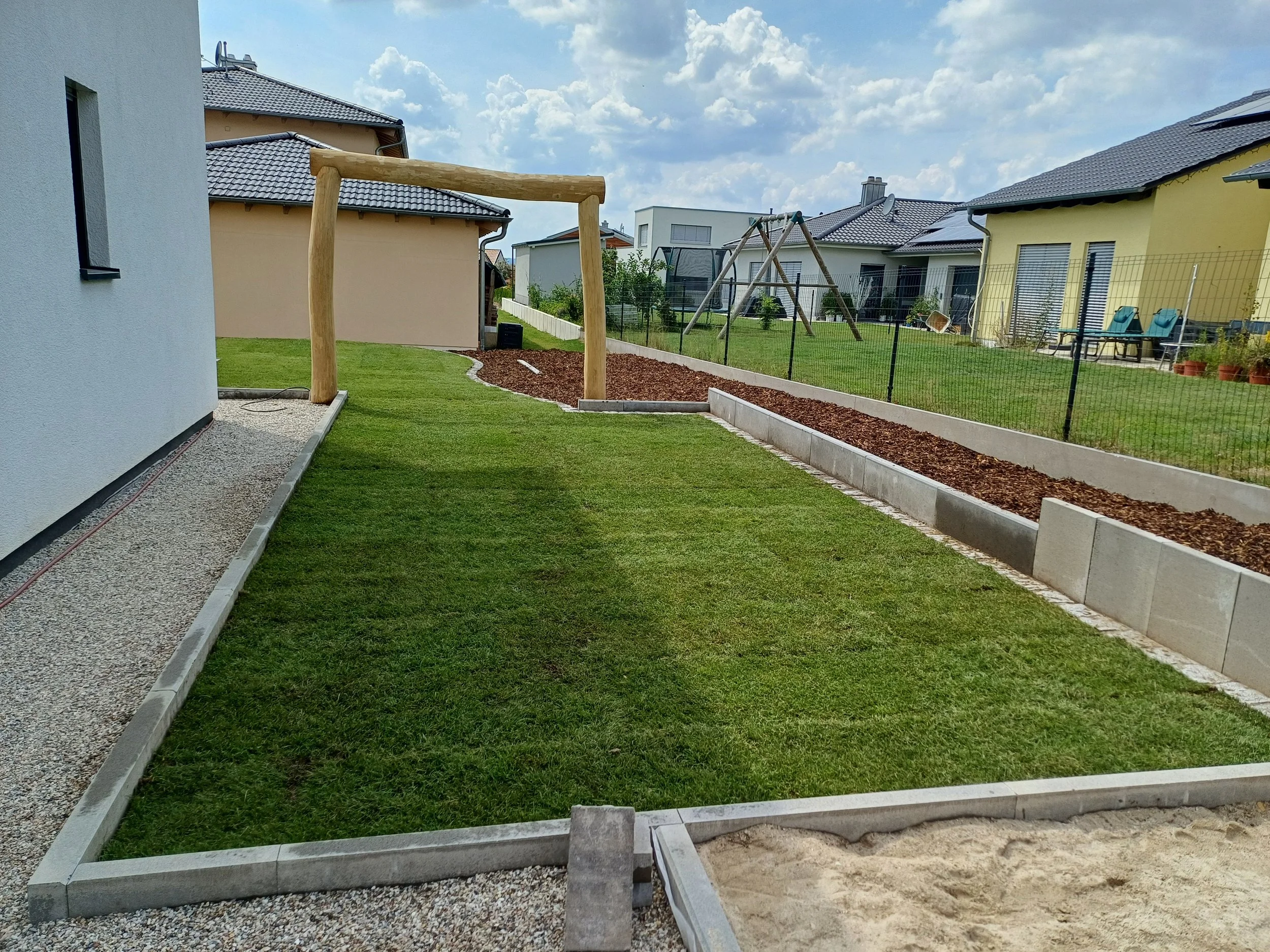 Garten mit Rasen, Gartenmöbeln, Schaukel und Gartenbeeten in einem Vorort, bewölkter Himmel.