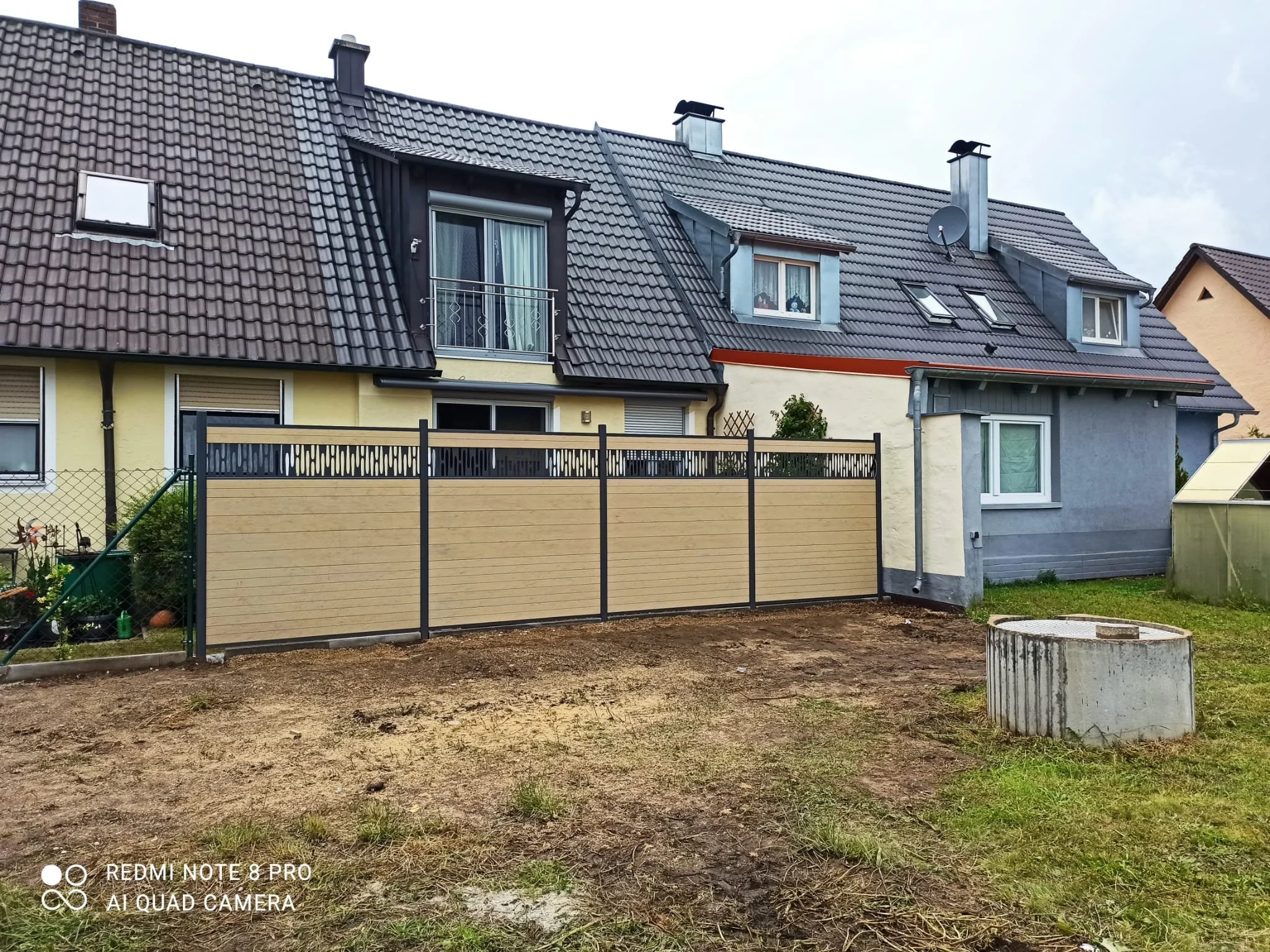 Ansicht eines Hauses mit Dachfenstern und Zaun, im Vordergrund ein leerer Gartenbereich.