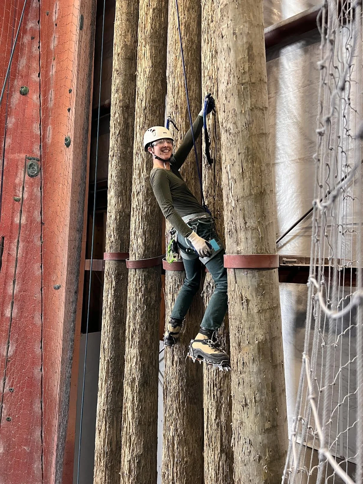 Climber learning ice climbing techniques on wooden poles indoors at Planet Rock