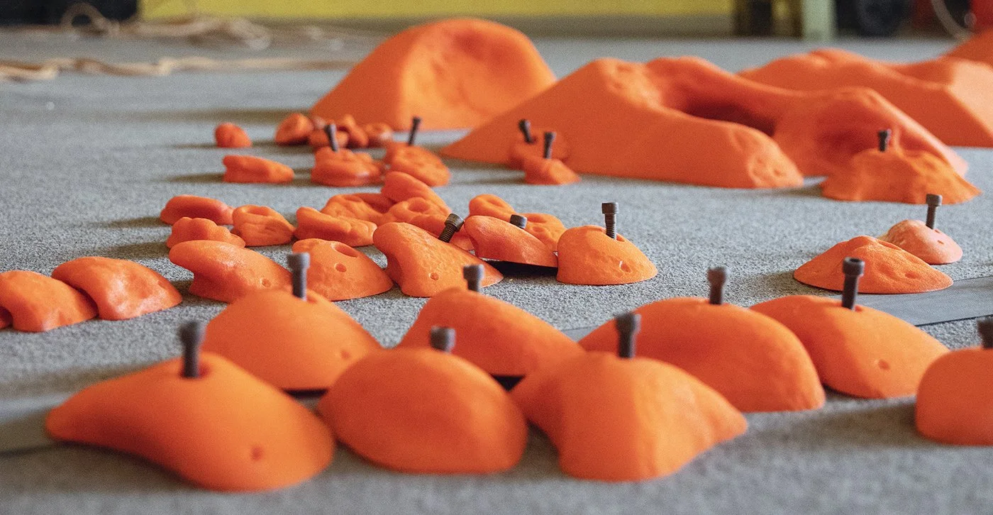 Orange climbing holds with bolts laying on the floor ready to be installed on the Planet Rock climbing walls