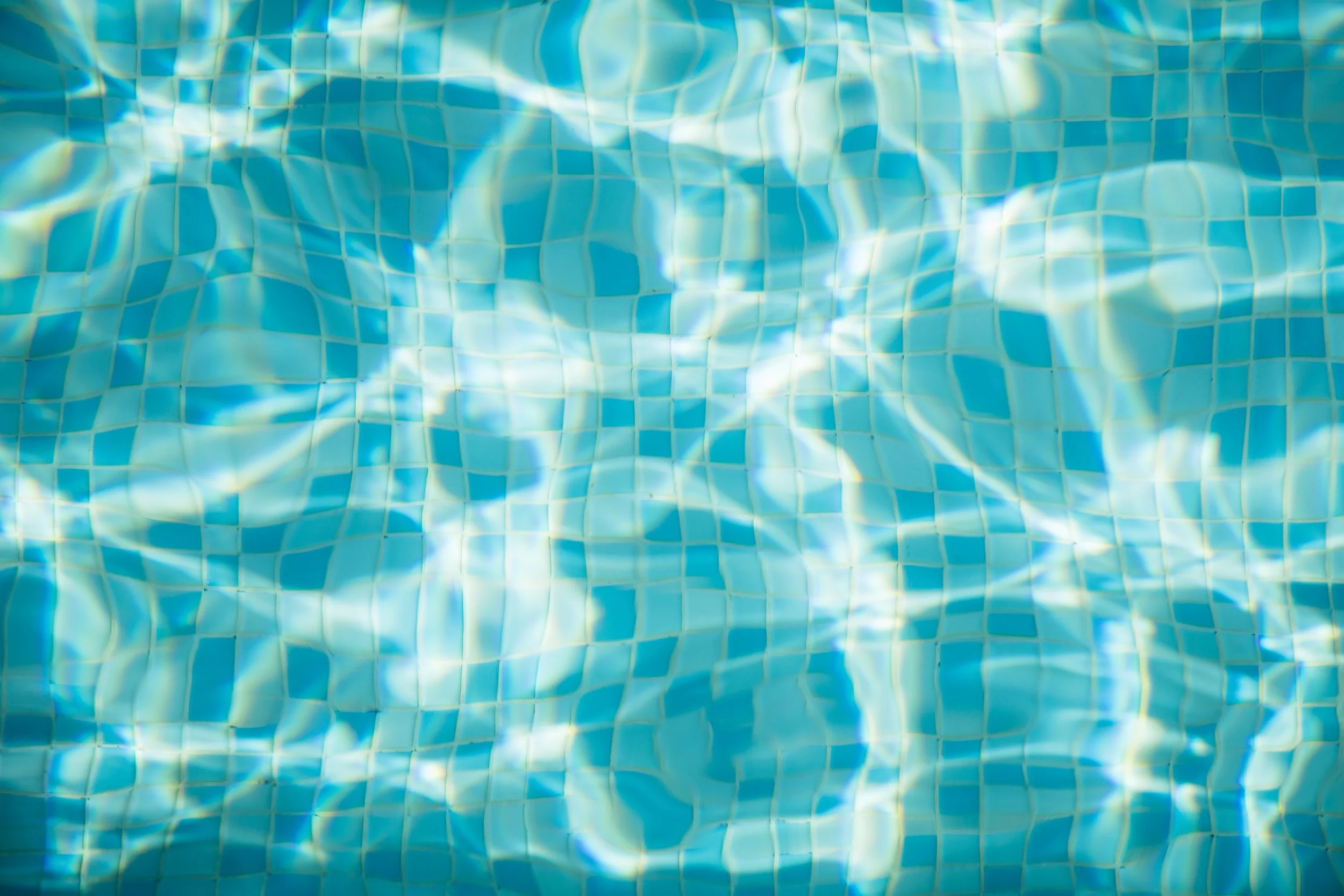 Close-up of a swimming pool's tiled bottom with sunlight reflecting on the water's surface.