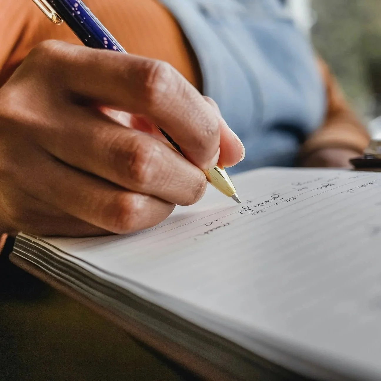 A hand holding a pen, poised over a writing pad.