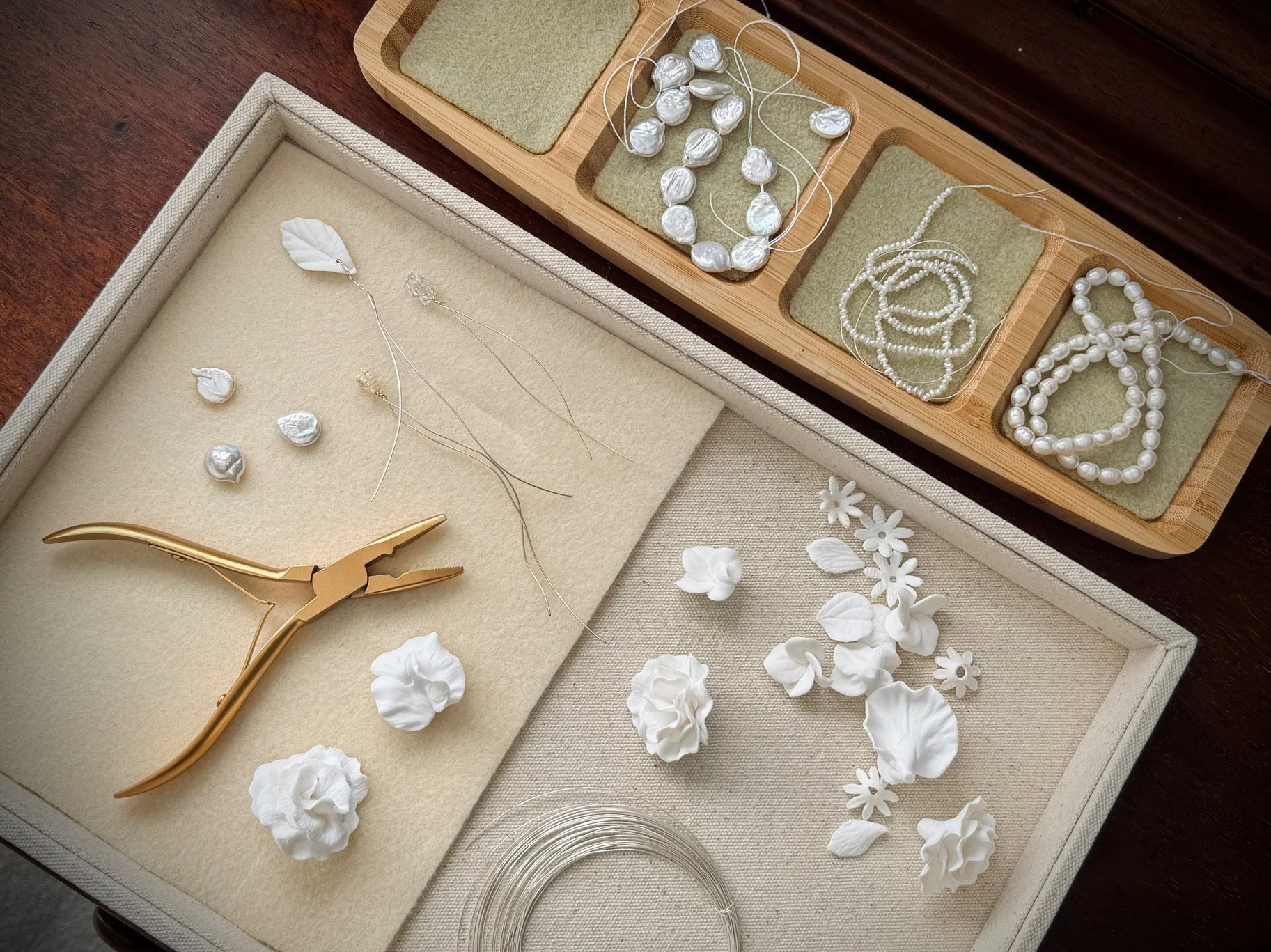 Flat lay of luxury bridal accessory materials including freshwater pearls, fine wire, handcrafted floral elements and jewellery tools, showcasing the design process behind bespoke bridal hair accessories.