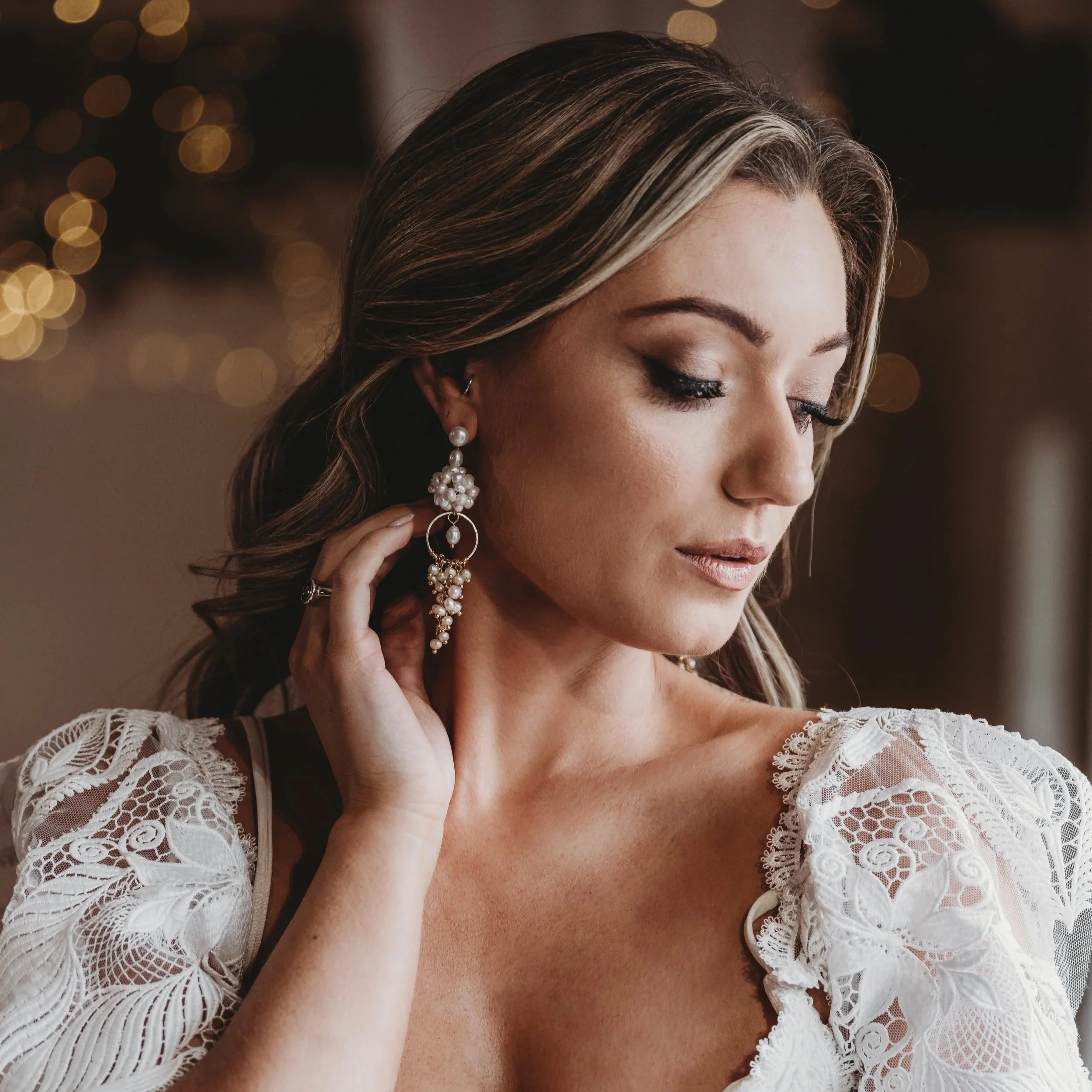 Bride wearing designer pearl bridal earrings by Jen Gilbert Bridal, styled with a lace wedding dress during bridal preparations