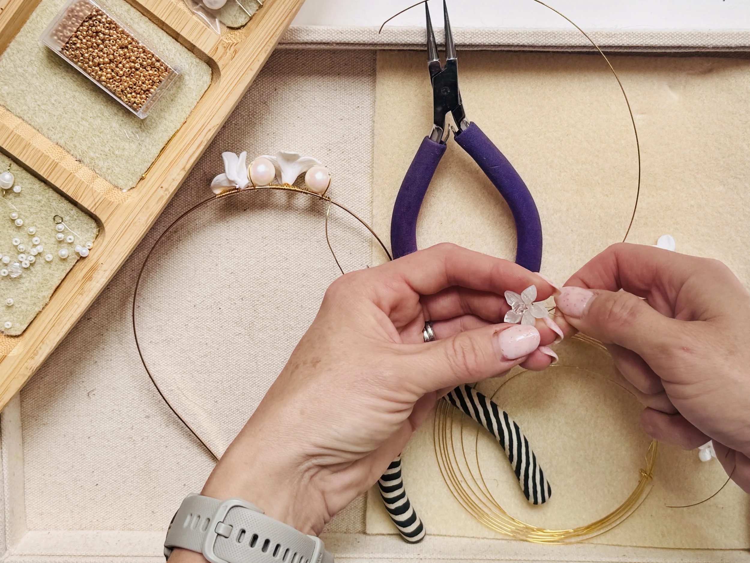 Hands of bridal accessory designer Jen Gilbert handcrafting a bespoke bridal headpiece using fine gold wire, pearls and delicate floral elements at her studio workbench.
