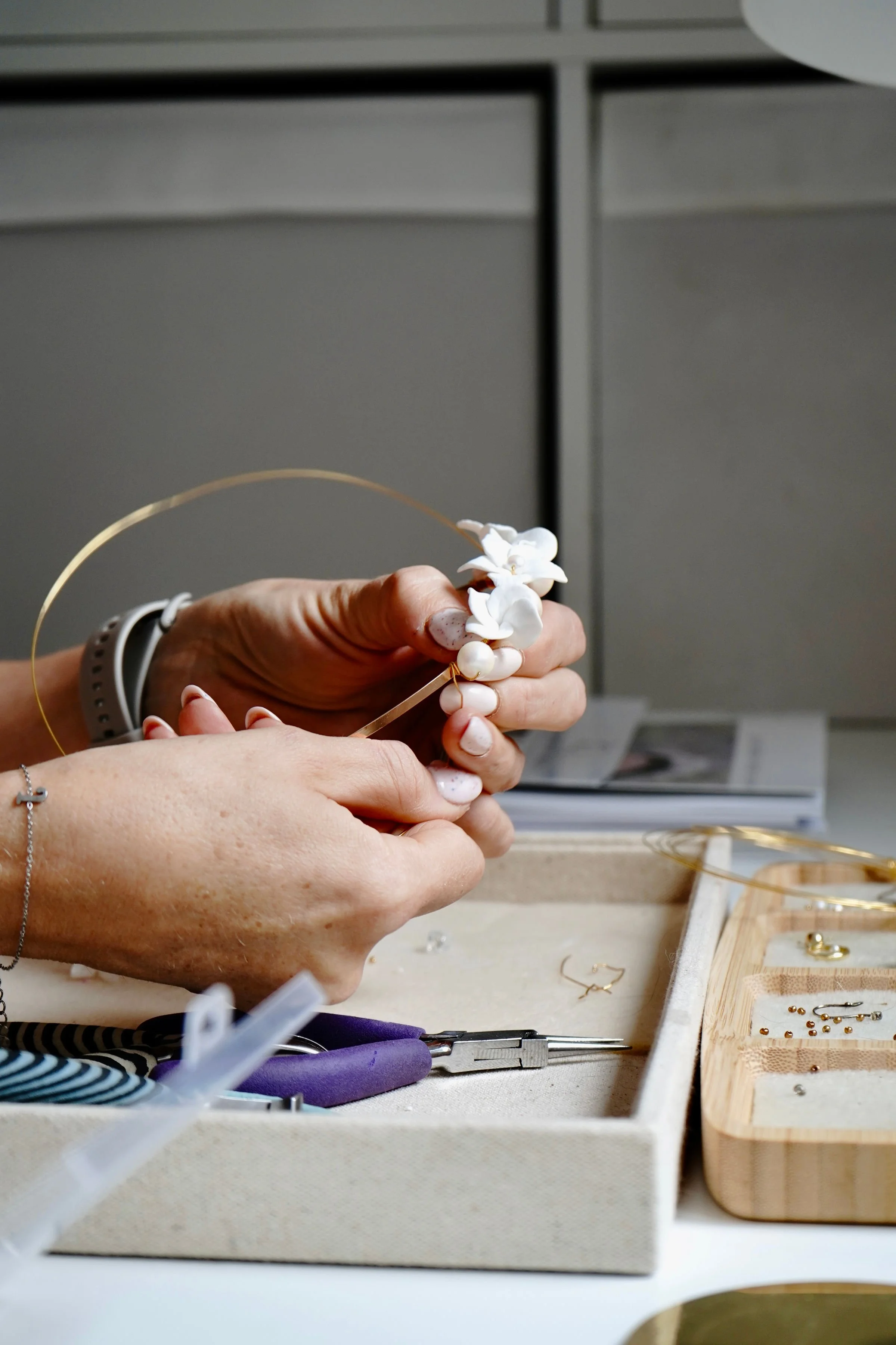 Hands of bridal accessory designer Jen Gilbert hand-crafting a floral pearl wedding hair accessory with gold wire, showing the bespoke design process.