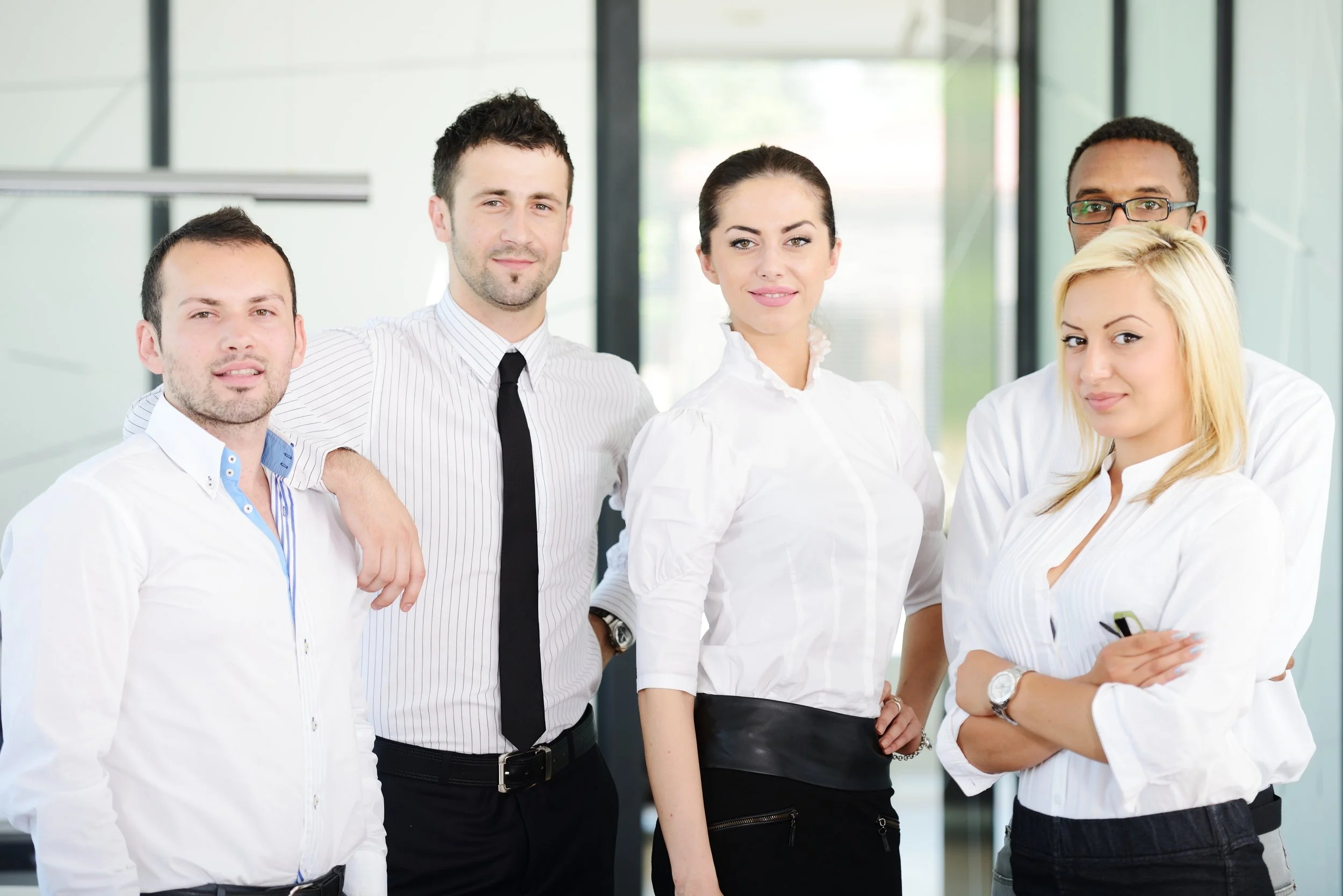 A diverse group of five professionally dressed people posing together in an office setting.