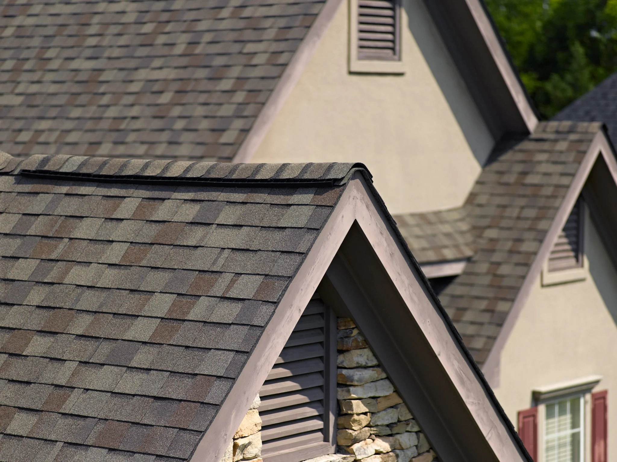 Close-up of rooftops with asphalt shingles, stone accents, and window shutters on a residential house.