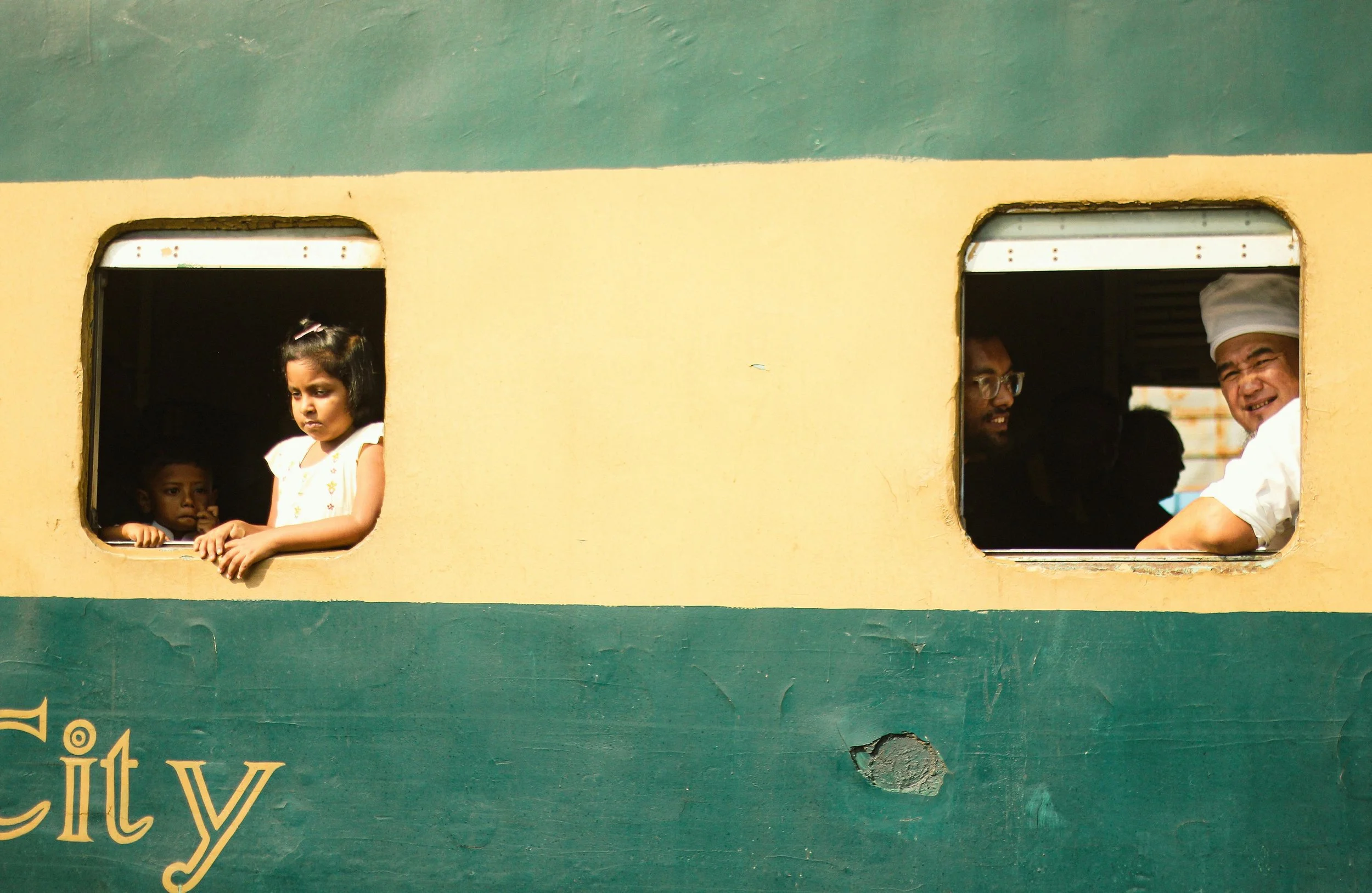 Children and adults looking out of the windows of a train with a yellow and green exterior.
