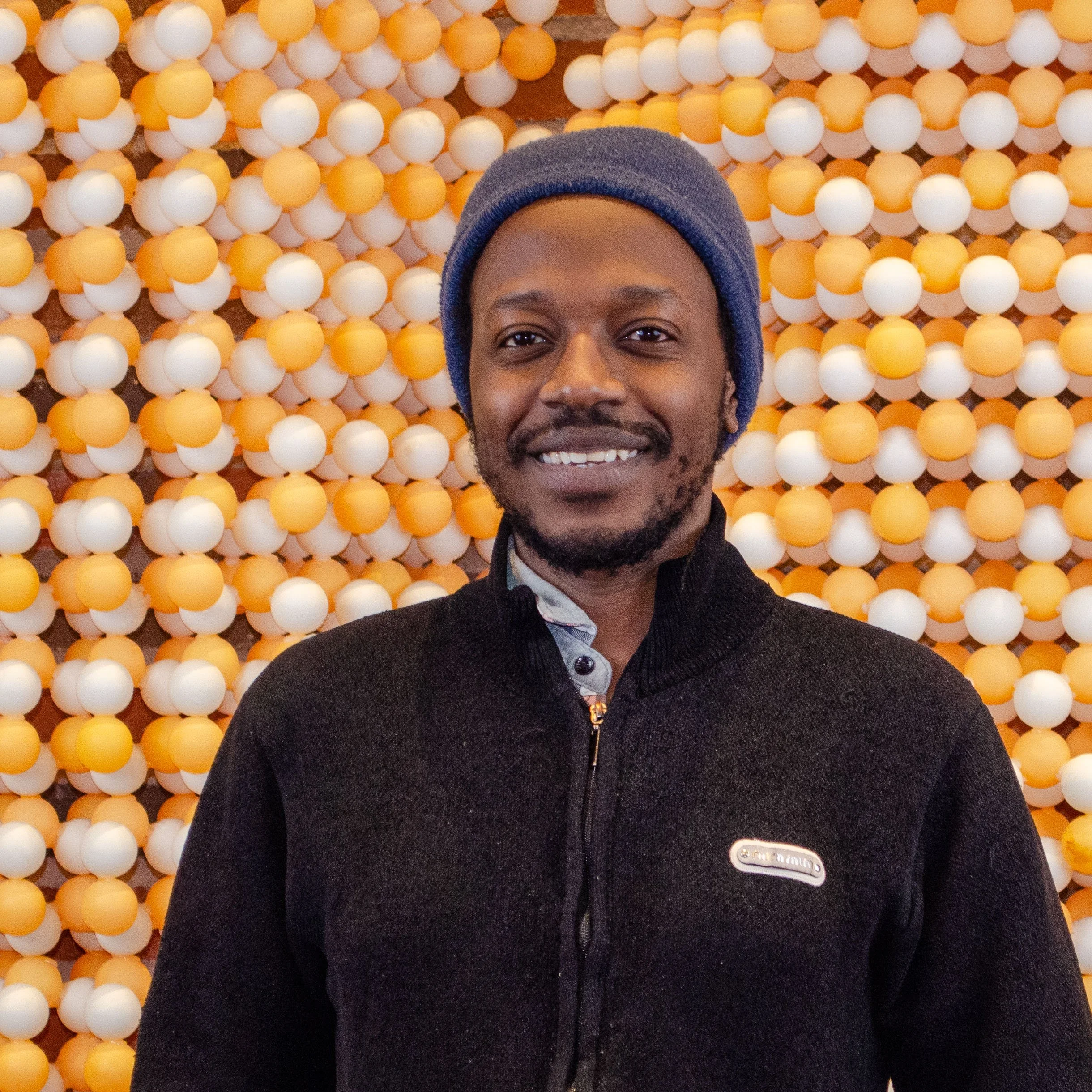 A man smiling in front of a wall decorated with orange and white golf balls.