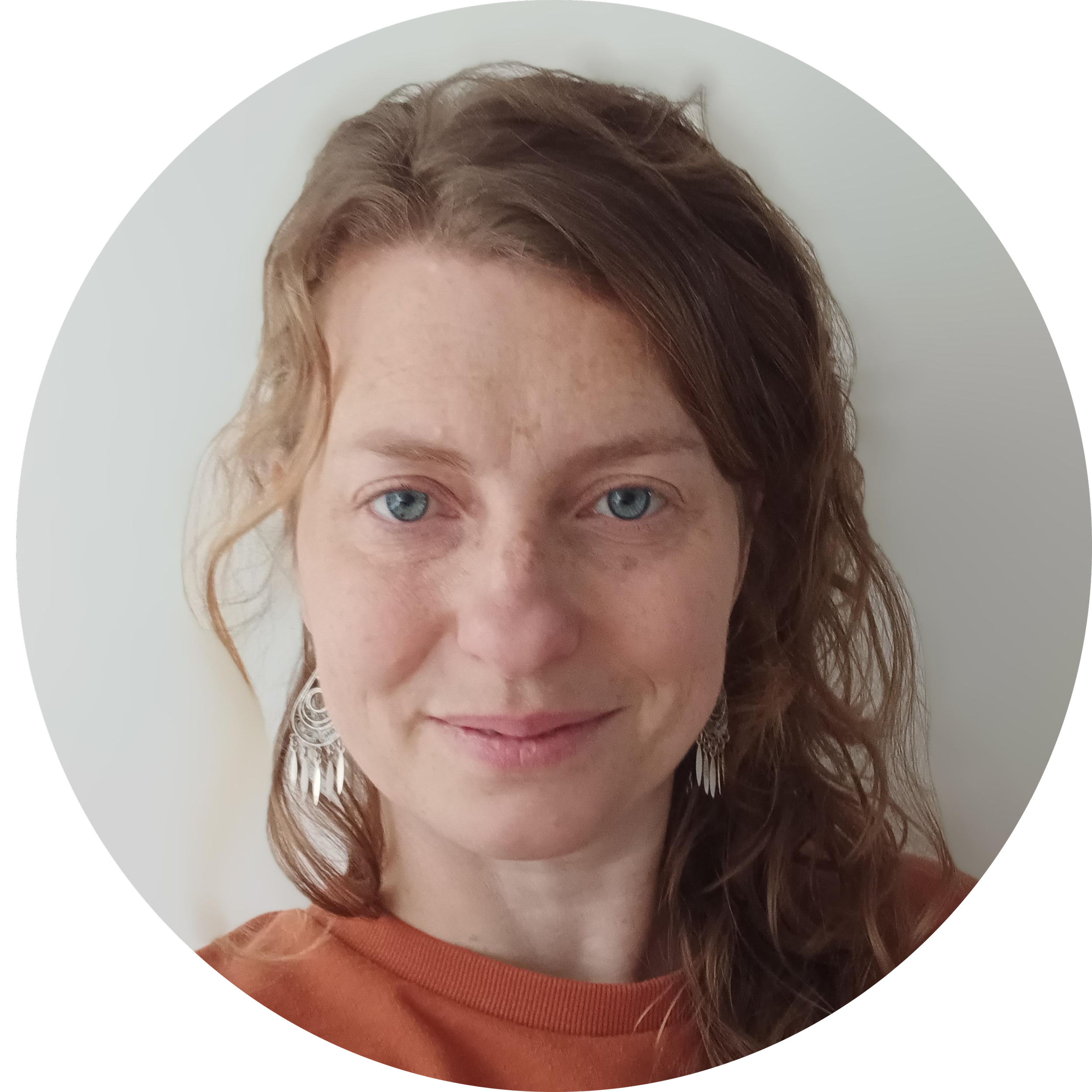 Becky Nel (tutor) long, wavy light brown hair, wearing a light-coloured sweater with a subtle pattern, sitting indoors near a window with a curtain.