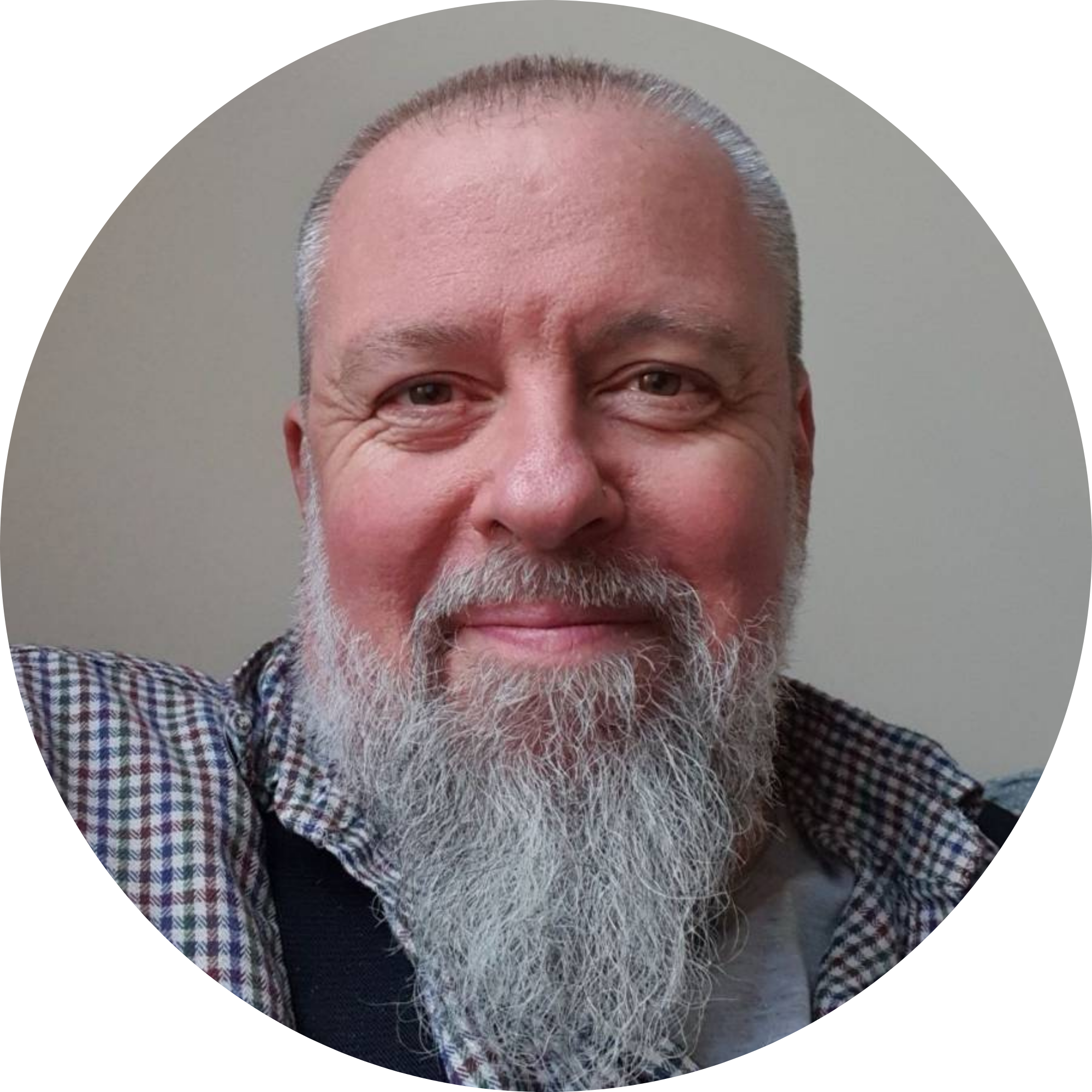 Close-up of a smiling older man with white beard and mustache, wearing a checkered shirt, against a plain background.