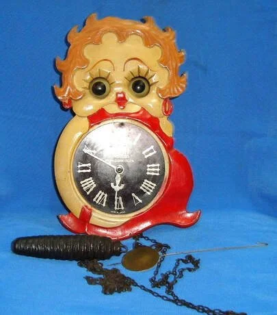 1930s Pendulum Wall Clock Probably one of the rarest clocks, it is similar to a cuckoo clock. Betty’s right arm wraps around the clock face and she is in what looks like an awkward half-sitting position. The pendulum extends below her legs. Clock fac