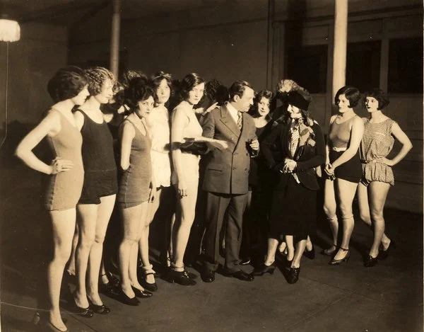 Max Fleischer (center) talking to his daughter, Ruth (wearing hat). Caption on reverse reads “Max Fleischer and a group of the prettiest chorus girls in New York, all of whom are engaged for his new series of two reel comedies, “Carrie of the Chorus.