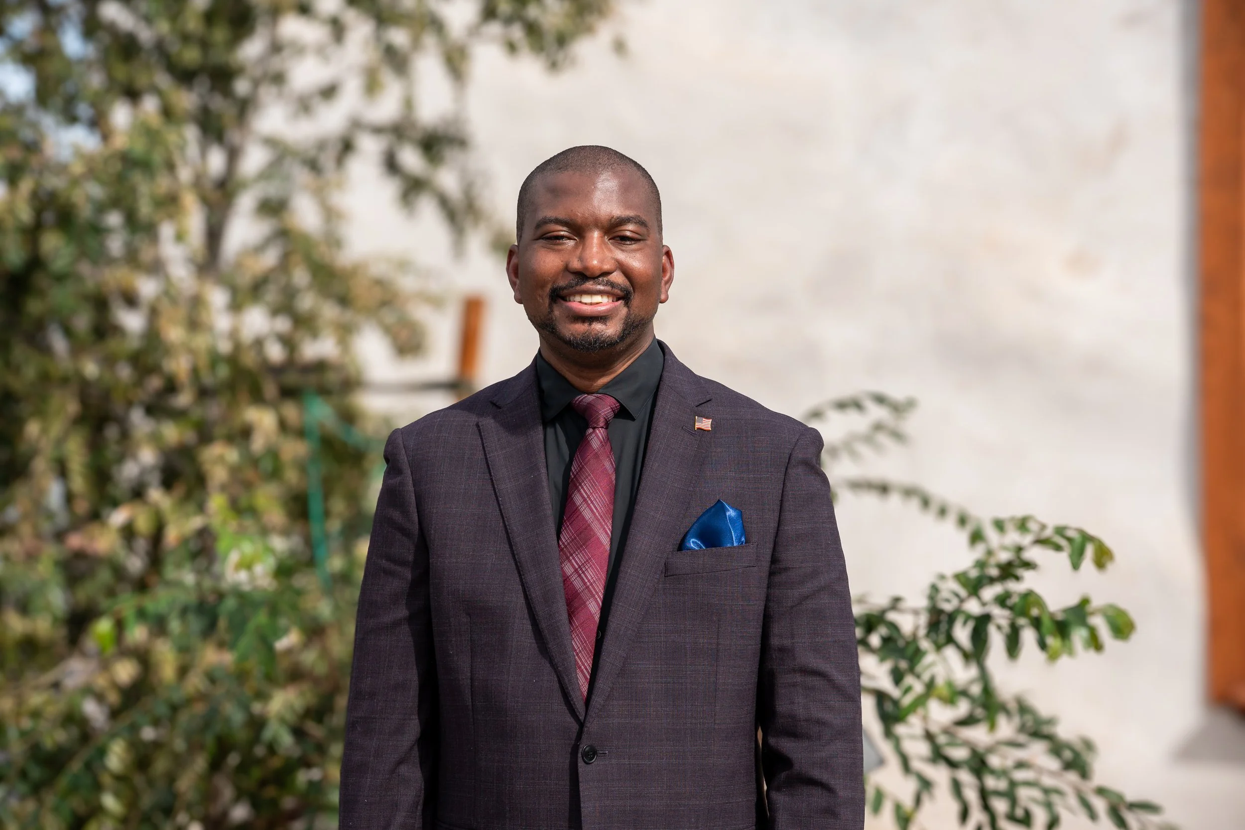 Man in a suit smiling outdoors during daytime.