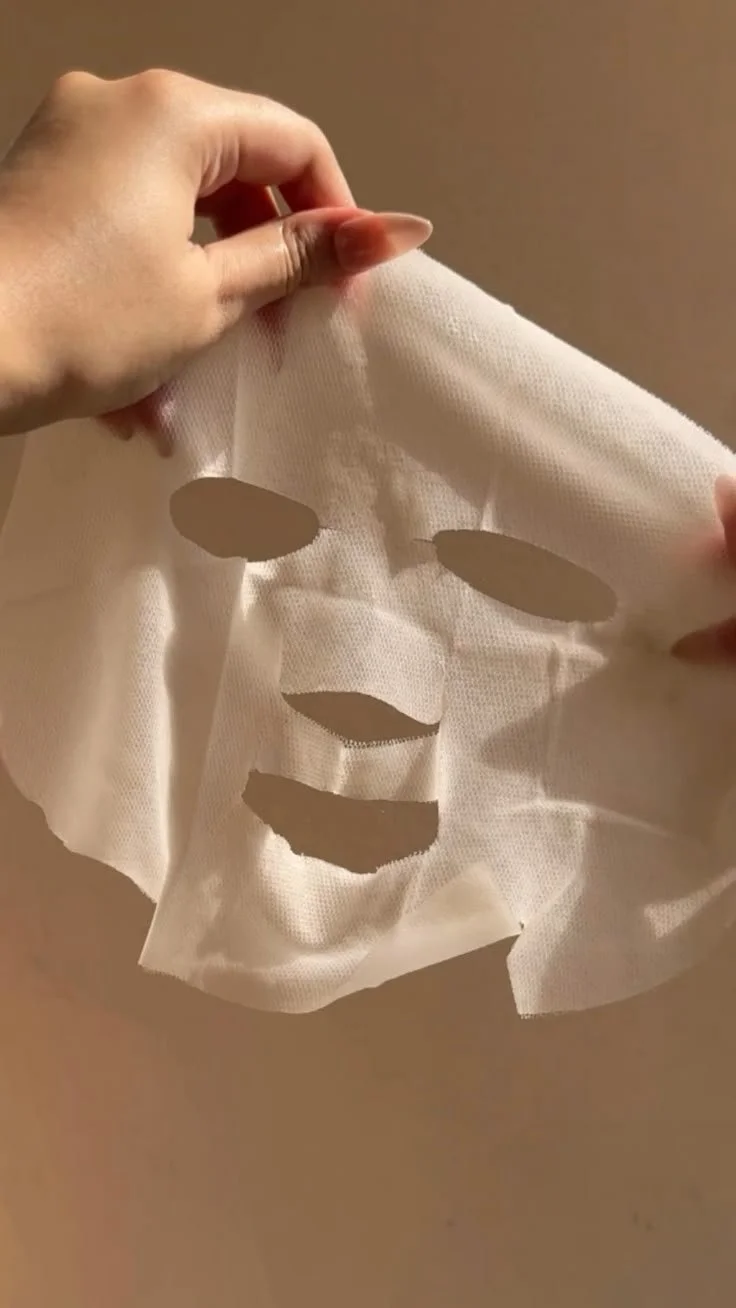 Person holding a white face mask with cutouts for eyes, nose, and mouth, made of cloth material.