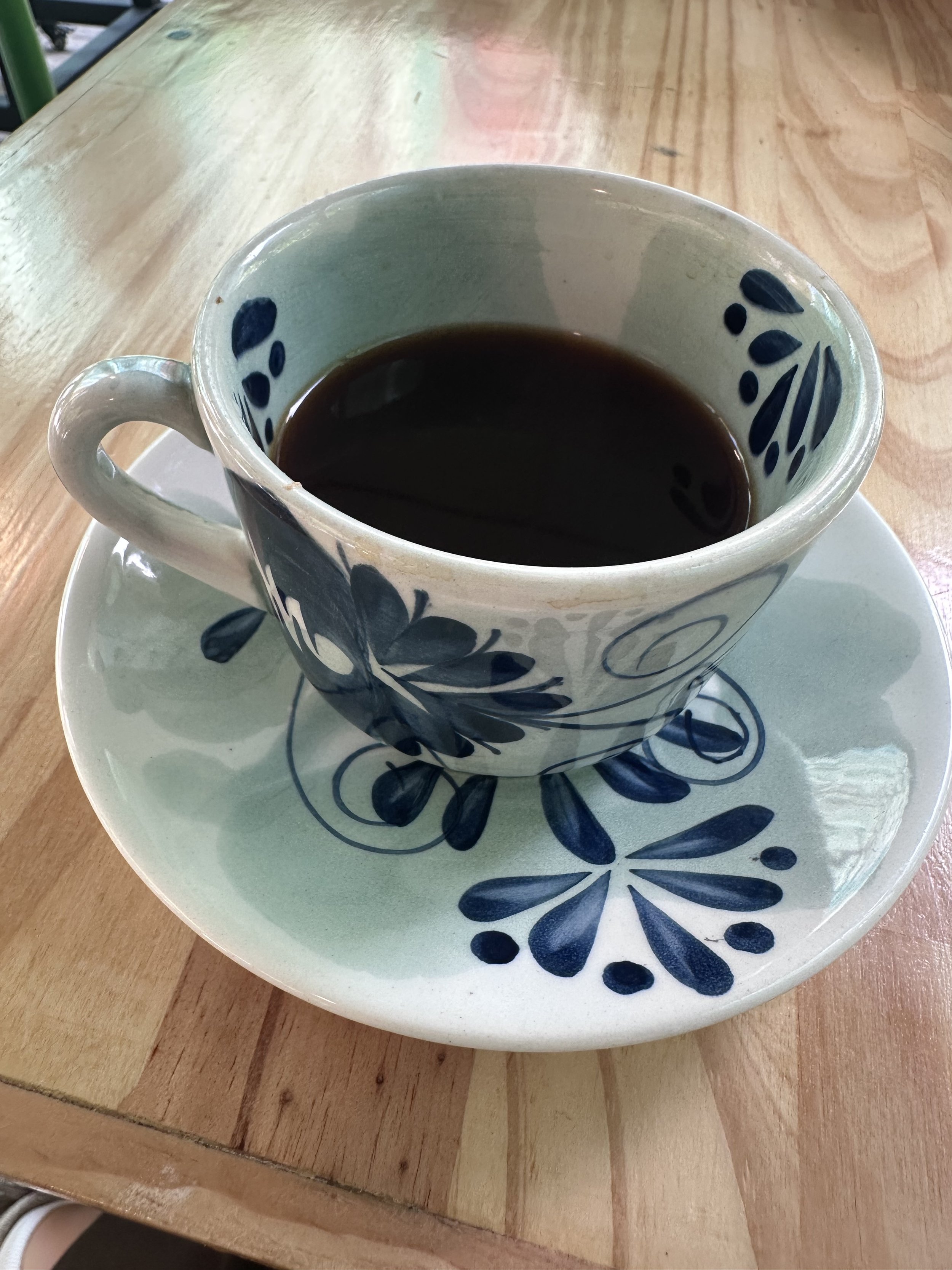 A cup of black coffee on a decorative saucer on a wooden table.