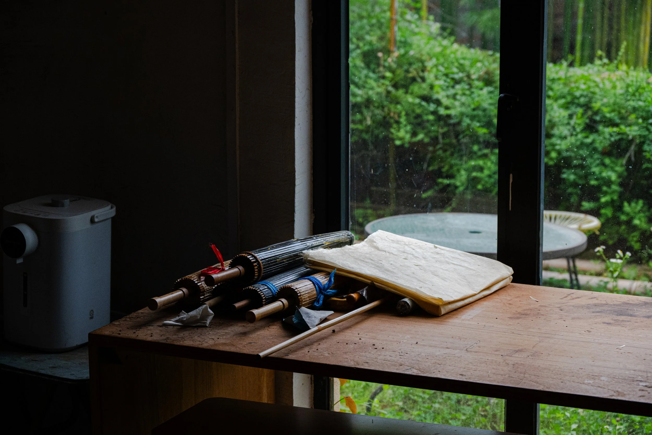 Musical instruments and sheet music on a wooden table by a window with a view of greenery outside