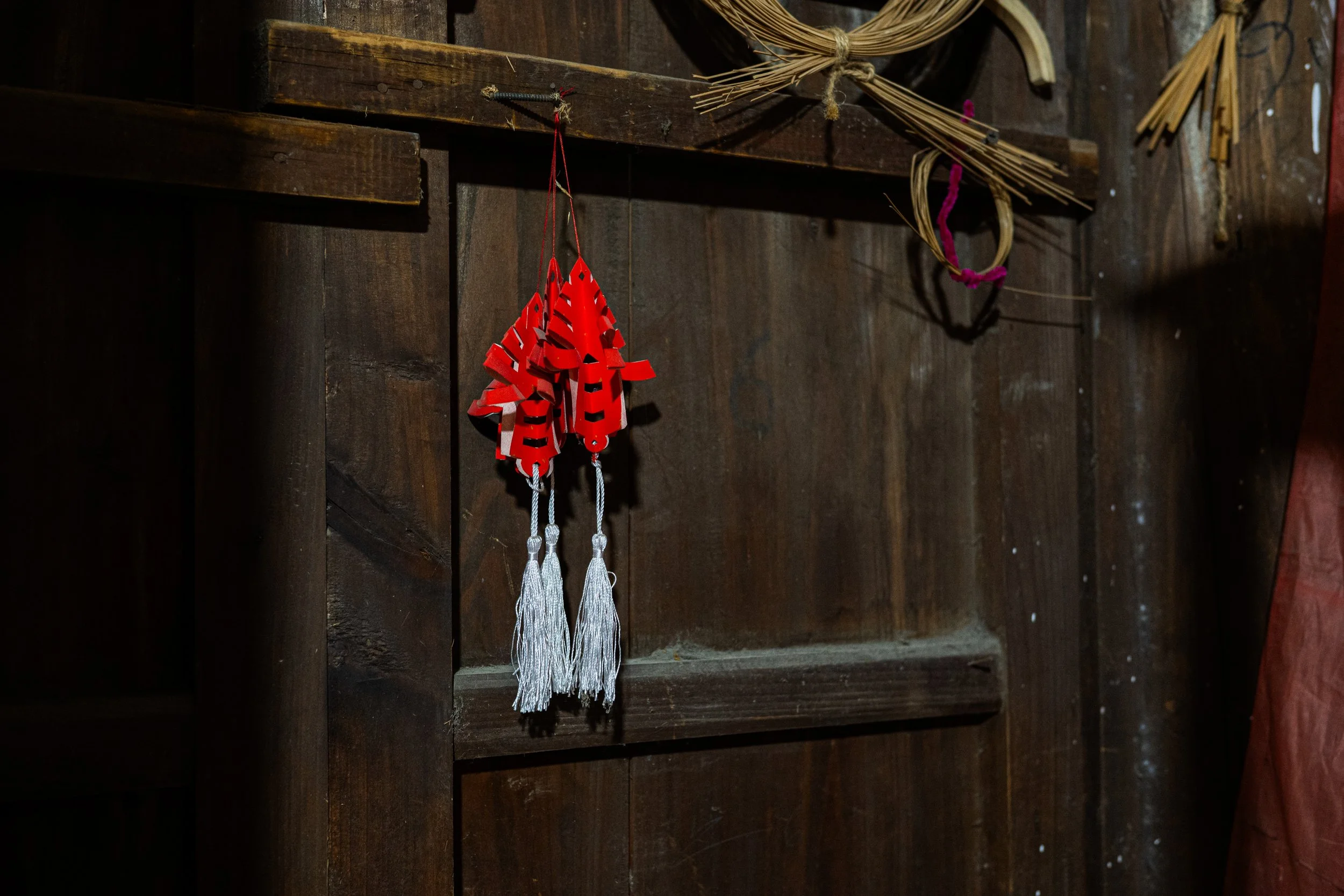 Red decorative hanging ornament with tassels, hanging on a dark wooden wall.