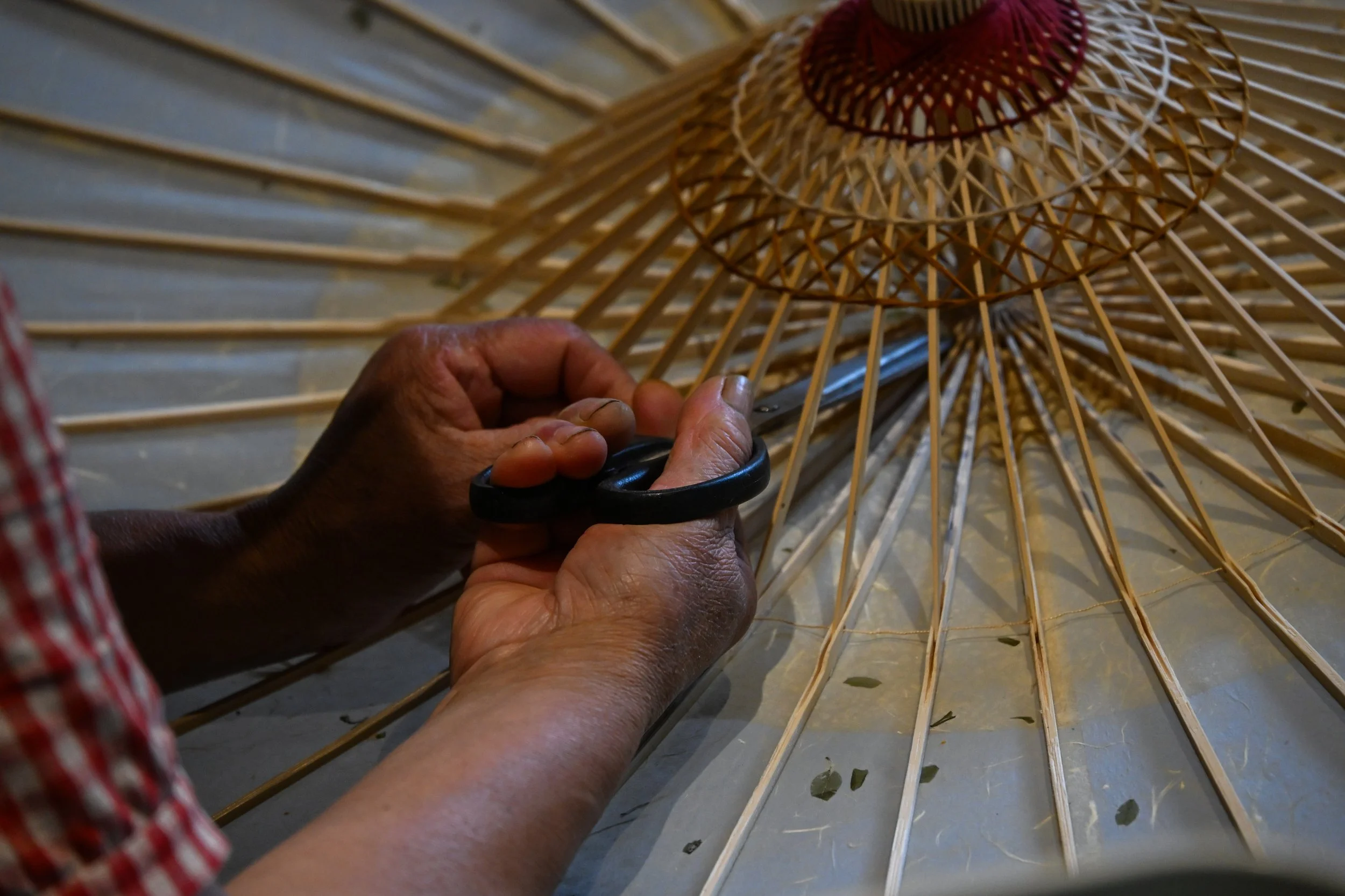 A person working on a large bamboo or wooden umbrella frame, using a tool to attach or adjust the radial spokes.