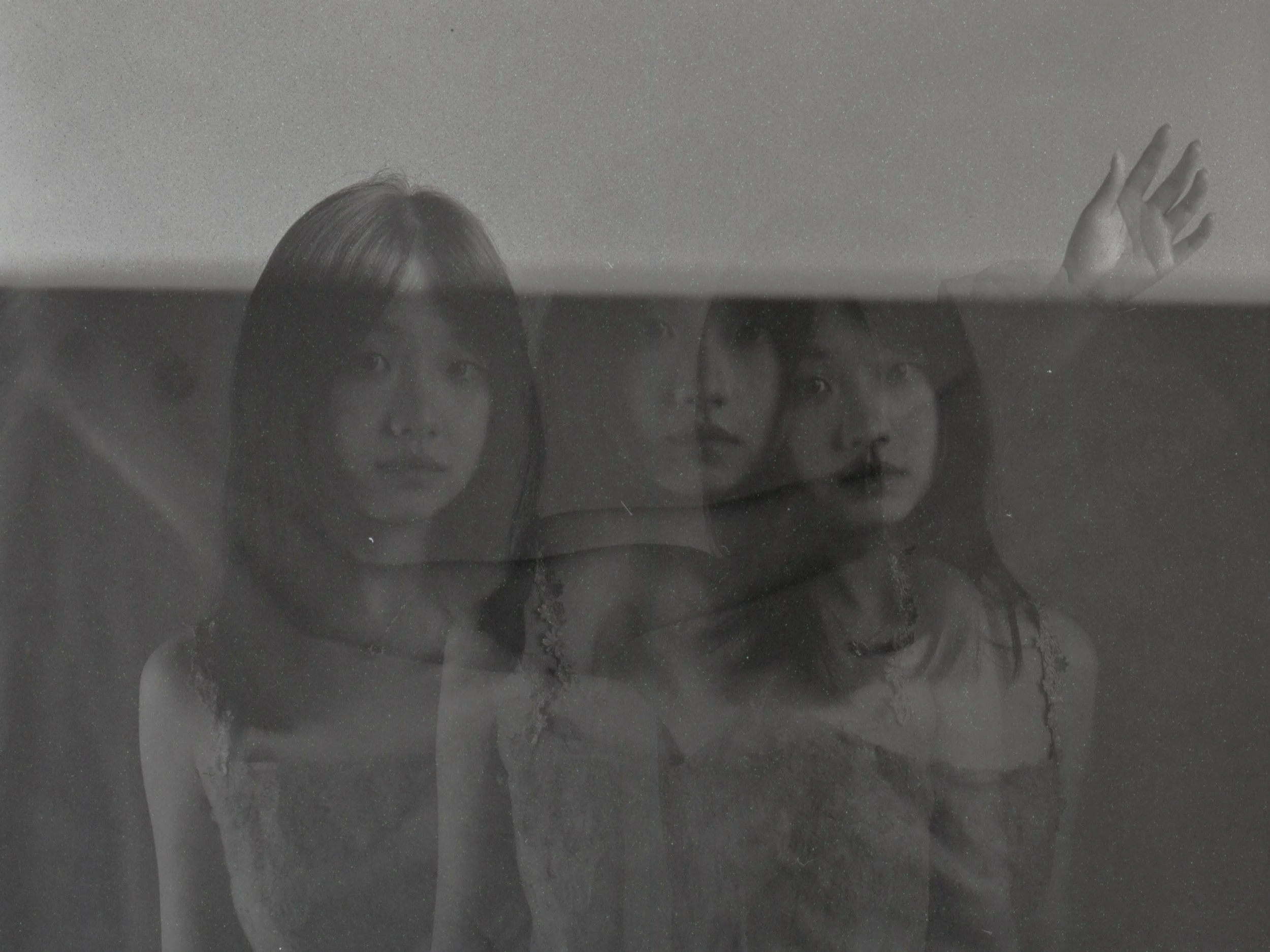 Black and white photo of three women, with one woman raising her hand, reflected in a glass surface.