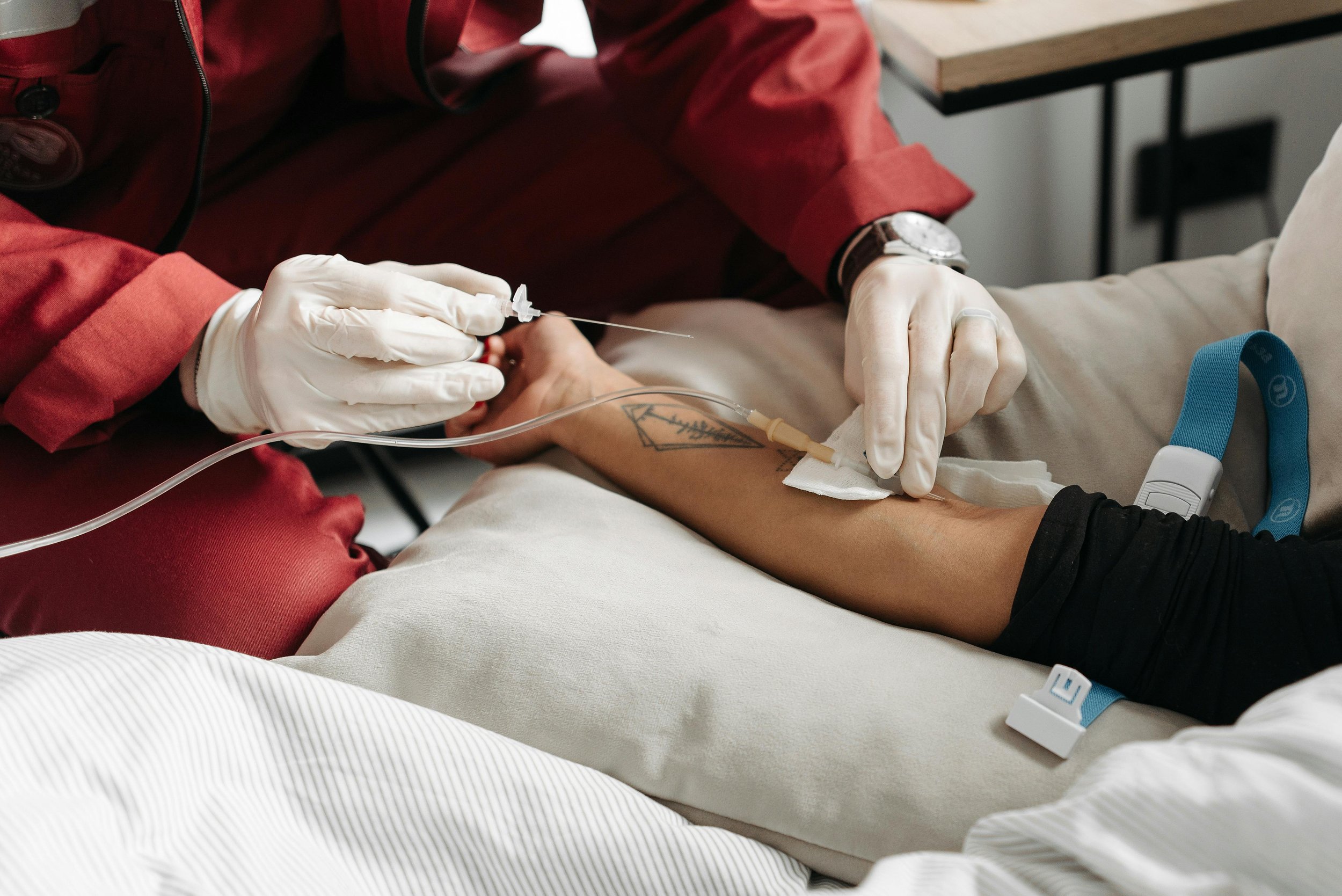 Medical professional administering intravenous therapy to a patient lying in a hospital bed.