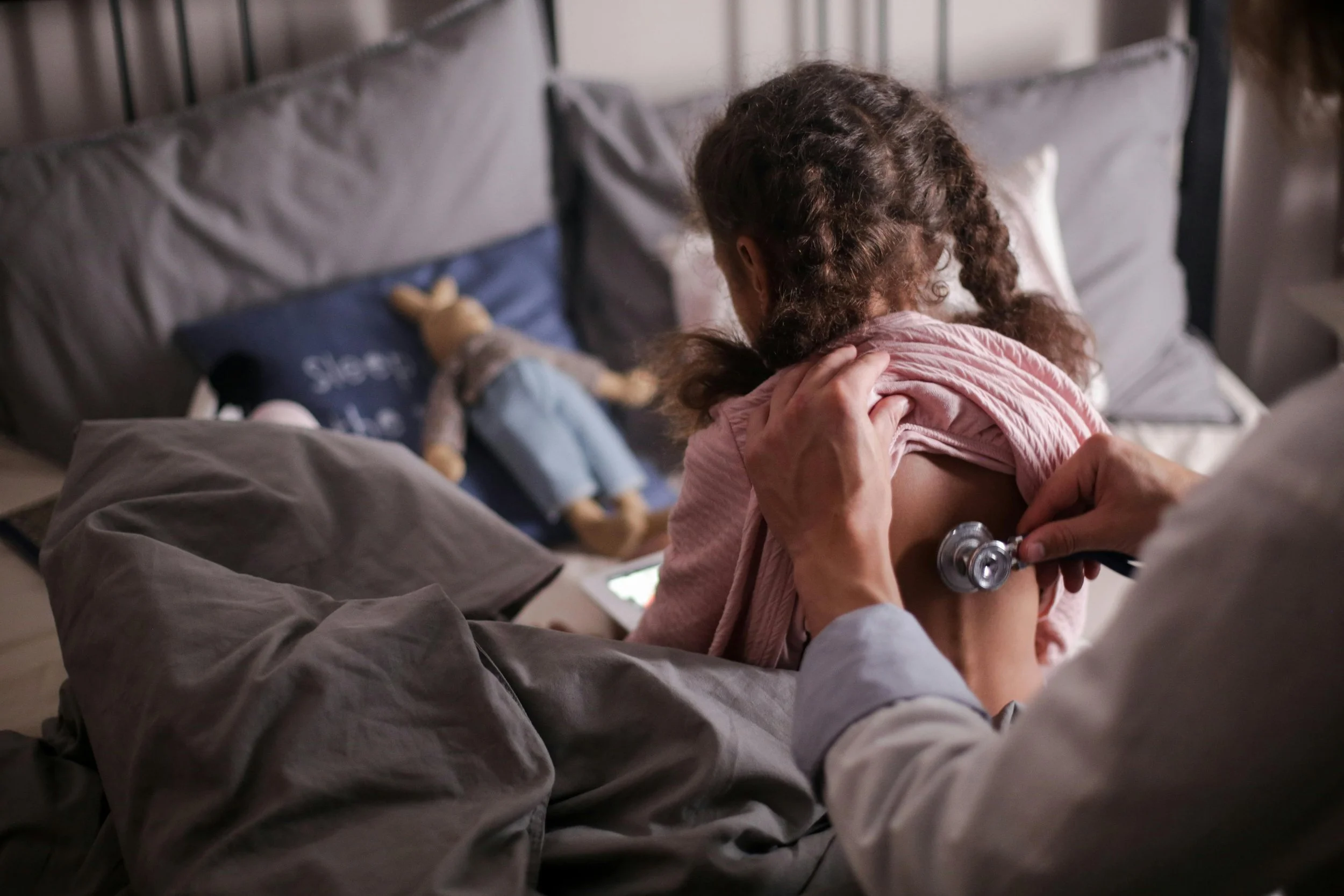 Doctor giving a vaccine shot to a young girl in a bedroom at home.