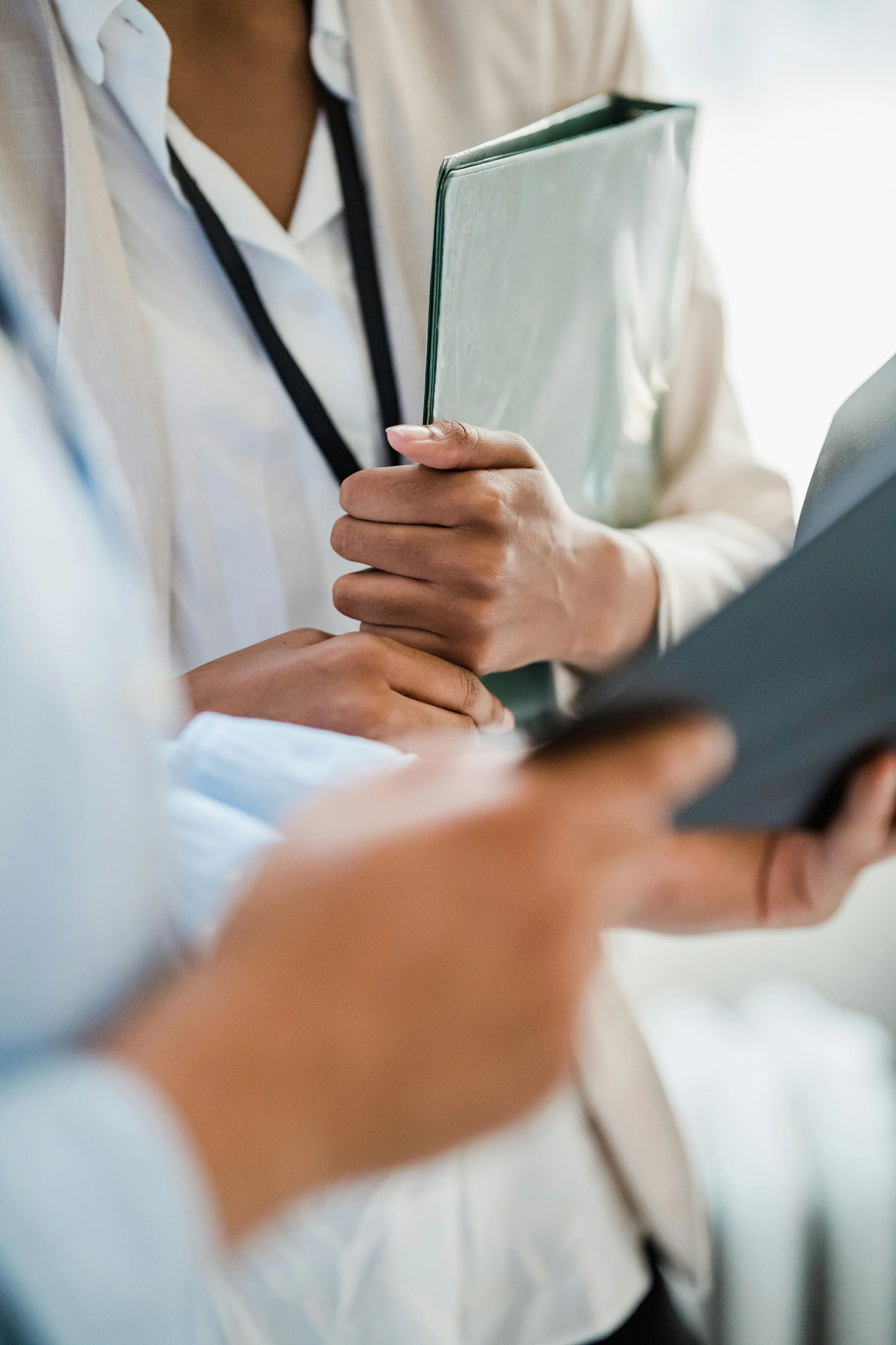 Close-up of professional individuals in business attire holding documents and tablets, engaging in a discussion.
