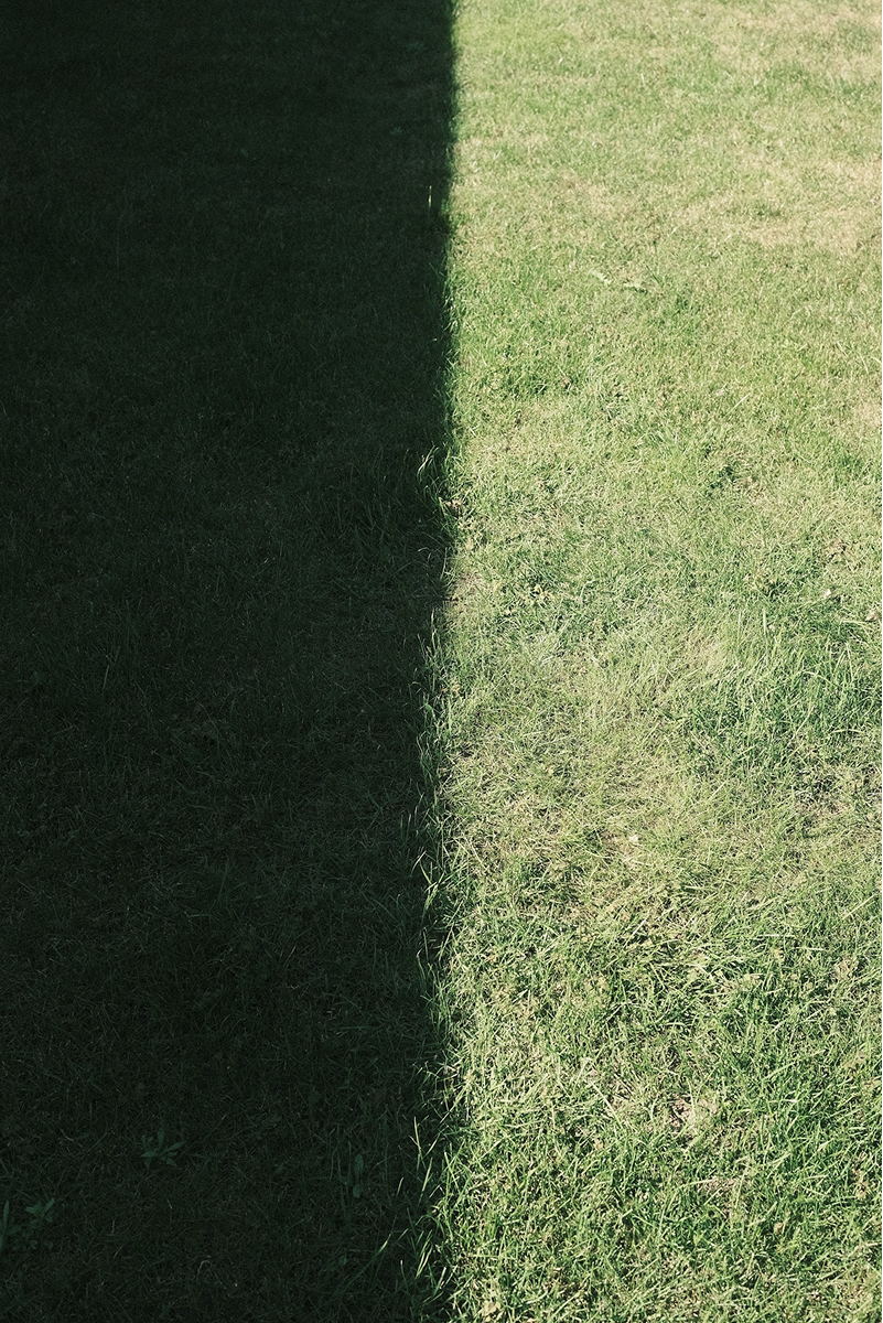 Shadow of a building cast on grass, with clear division between shaded and sunlit areas.