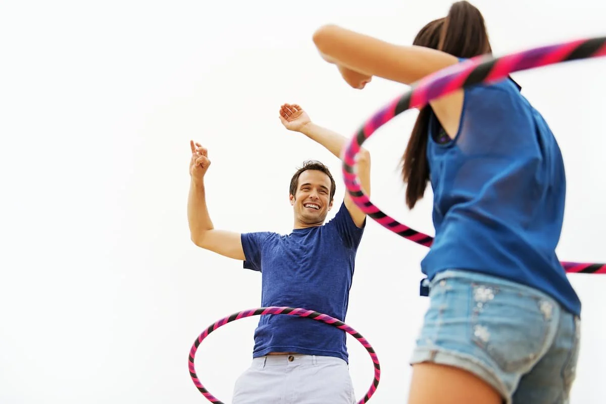 A man and woman outdoors playing with hula hoops against a white sky.