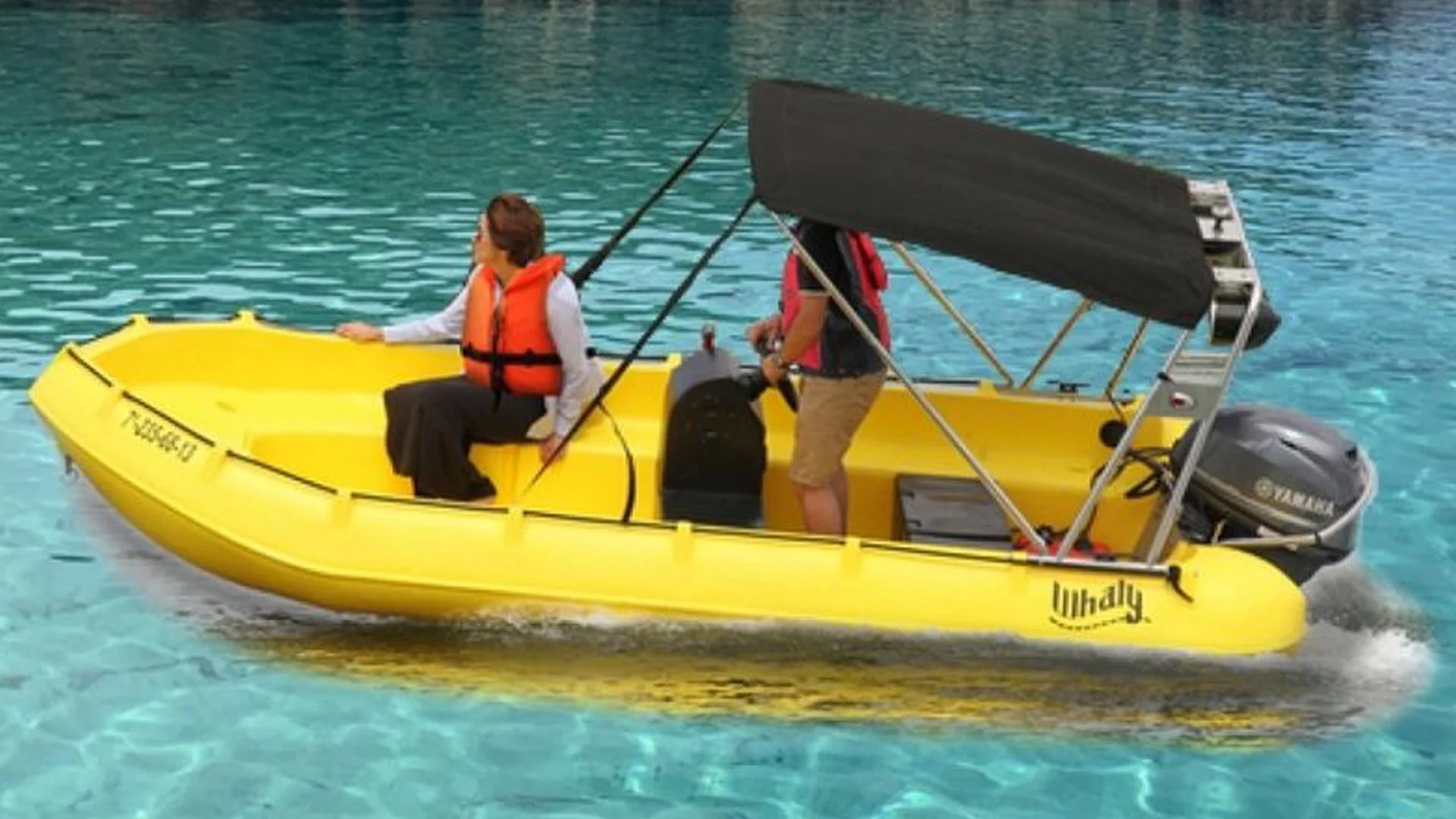 Yellow boat on water with two people: one sitting and the other standing, both wearing life jackets, with a black canopy and an outboard motor.