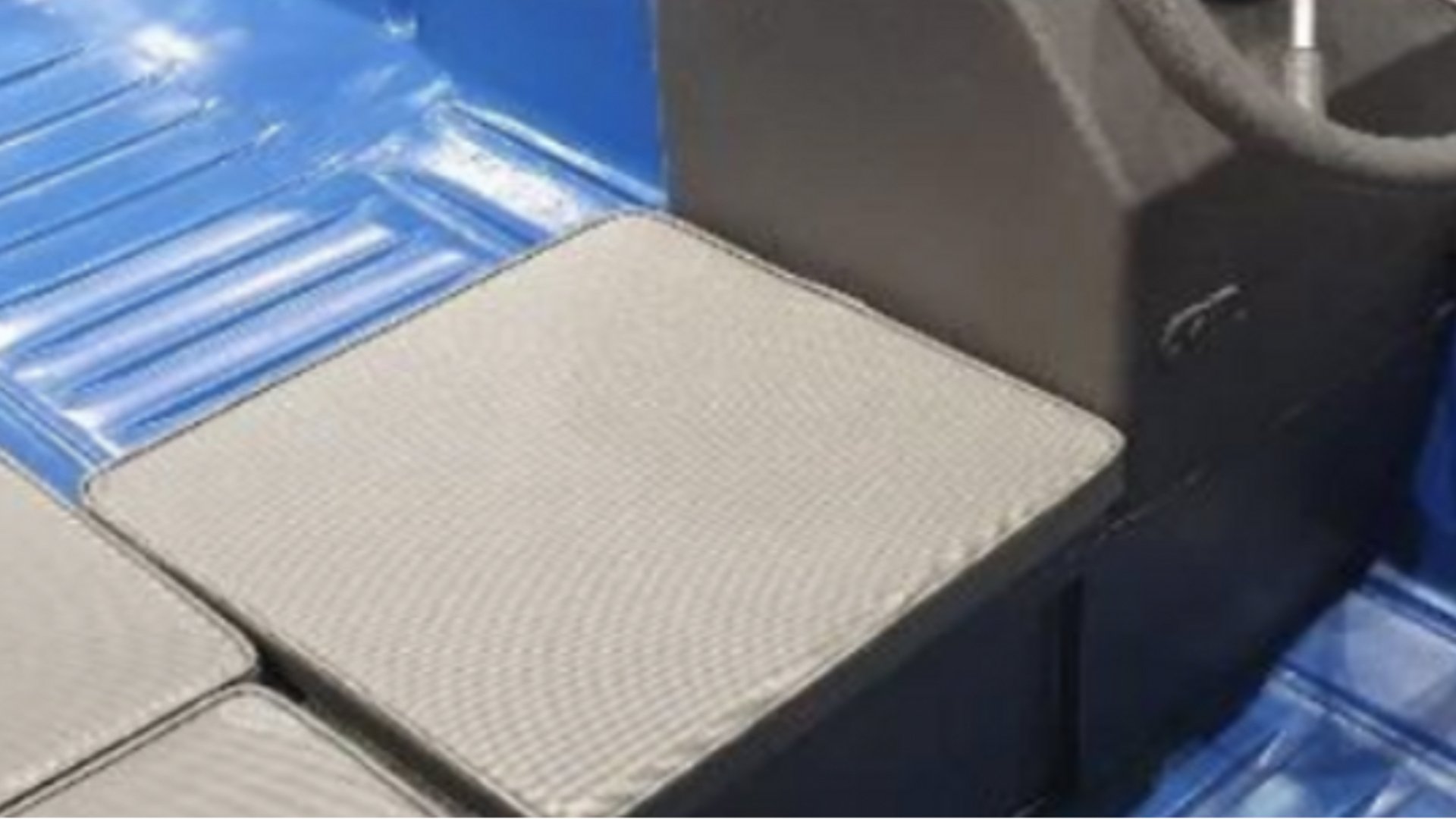 Close-up of a gaming console, controller, and empty beige cushions on a black surface, with blue tiled flooring in the background.