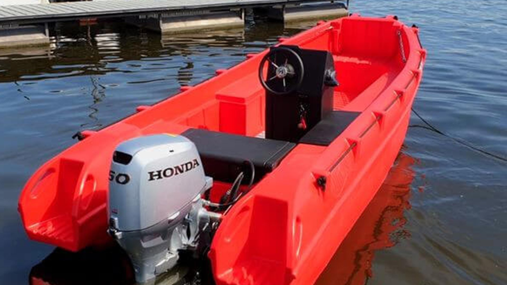 A small red boat with a Honda outboard motor, located on the water near a dock.