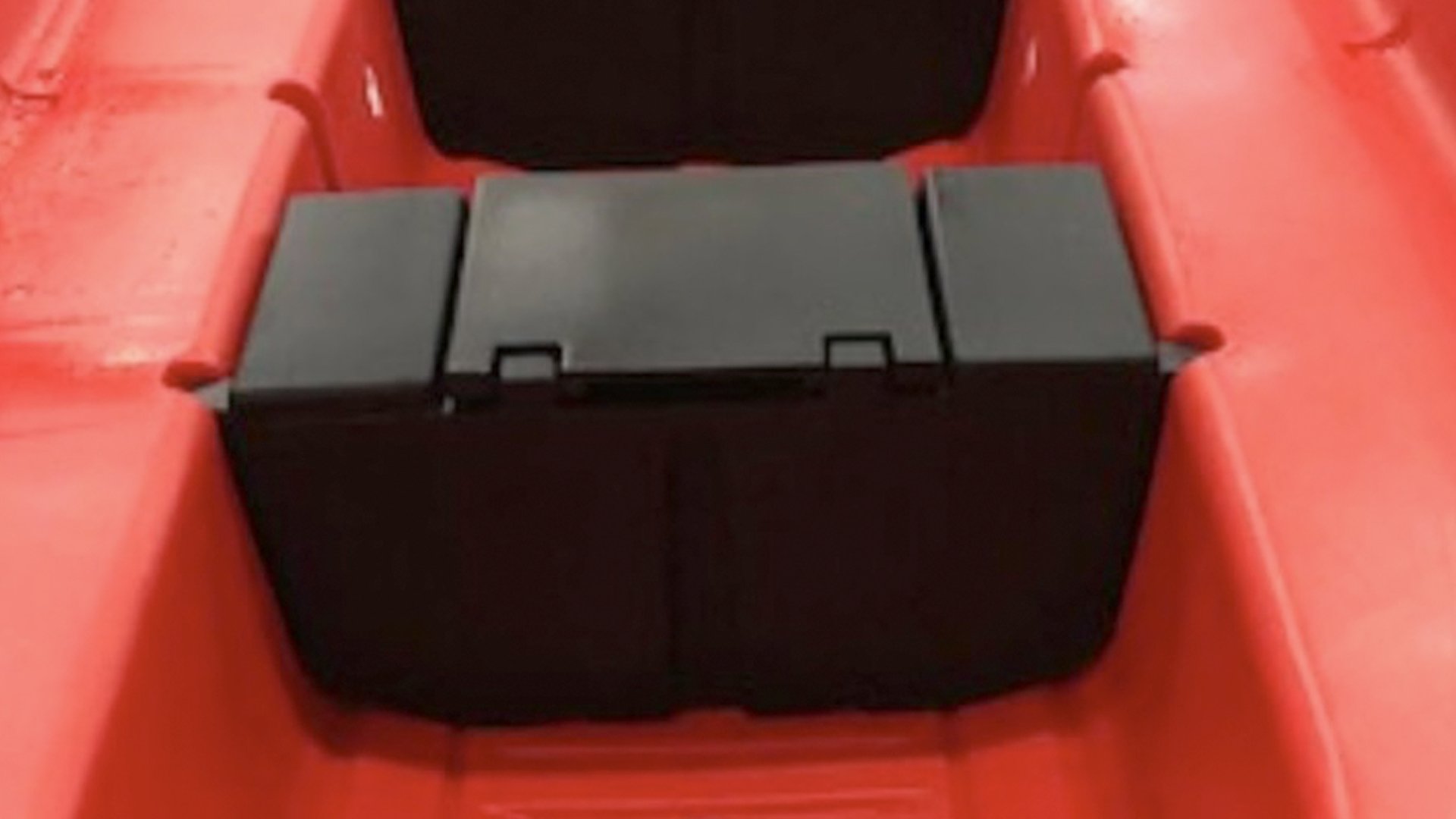 Close-up of a black rectangular object placed inside a red plastic boat or kayak.
