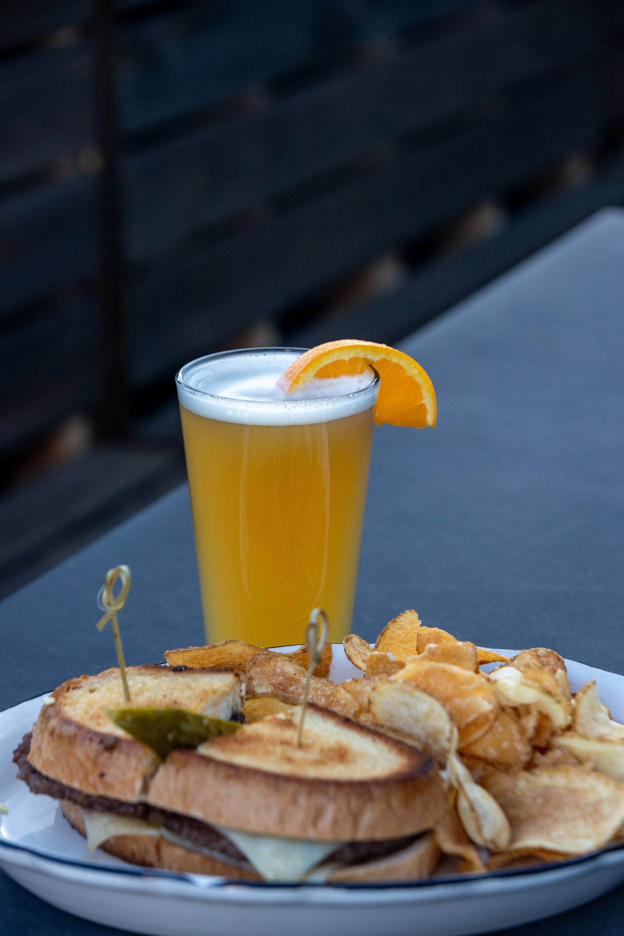 A plate with a sandwich and potato chips next to a tall glass of orange juice garnished with an orange slice.