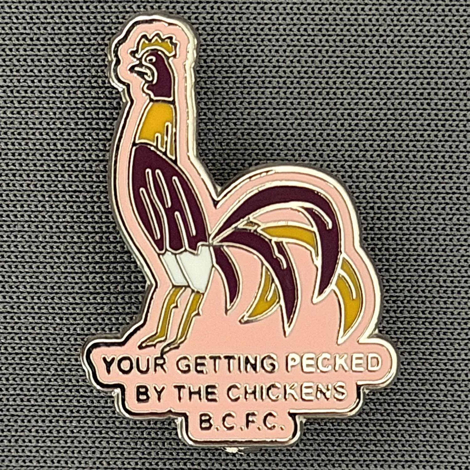 Reference Number: BCBAN065
Size: H 24.7 mm x W 17.9 mm
Pin Type: Brooch Pin
Plating: Silver
Value: £6
Manufacturer: Unknown
Comments: Pink, Claret & Amber Bantam, Pecked By The Chickens 