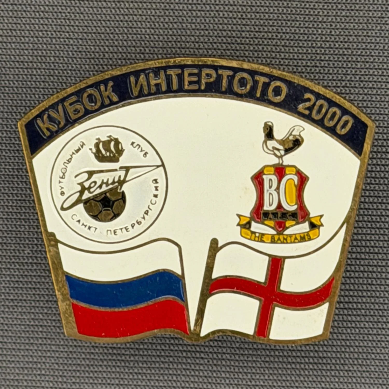 Reference Number: BCRUS028
Size: H 26 mm x W 32.3 mm
Pin Type: Metal Clutch
Plating: Antique Gold
Value: £12
Manufacturer: Unknown
Comments: Zenit St. Petersburg Inter Toto Cup, Black Top, White Background