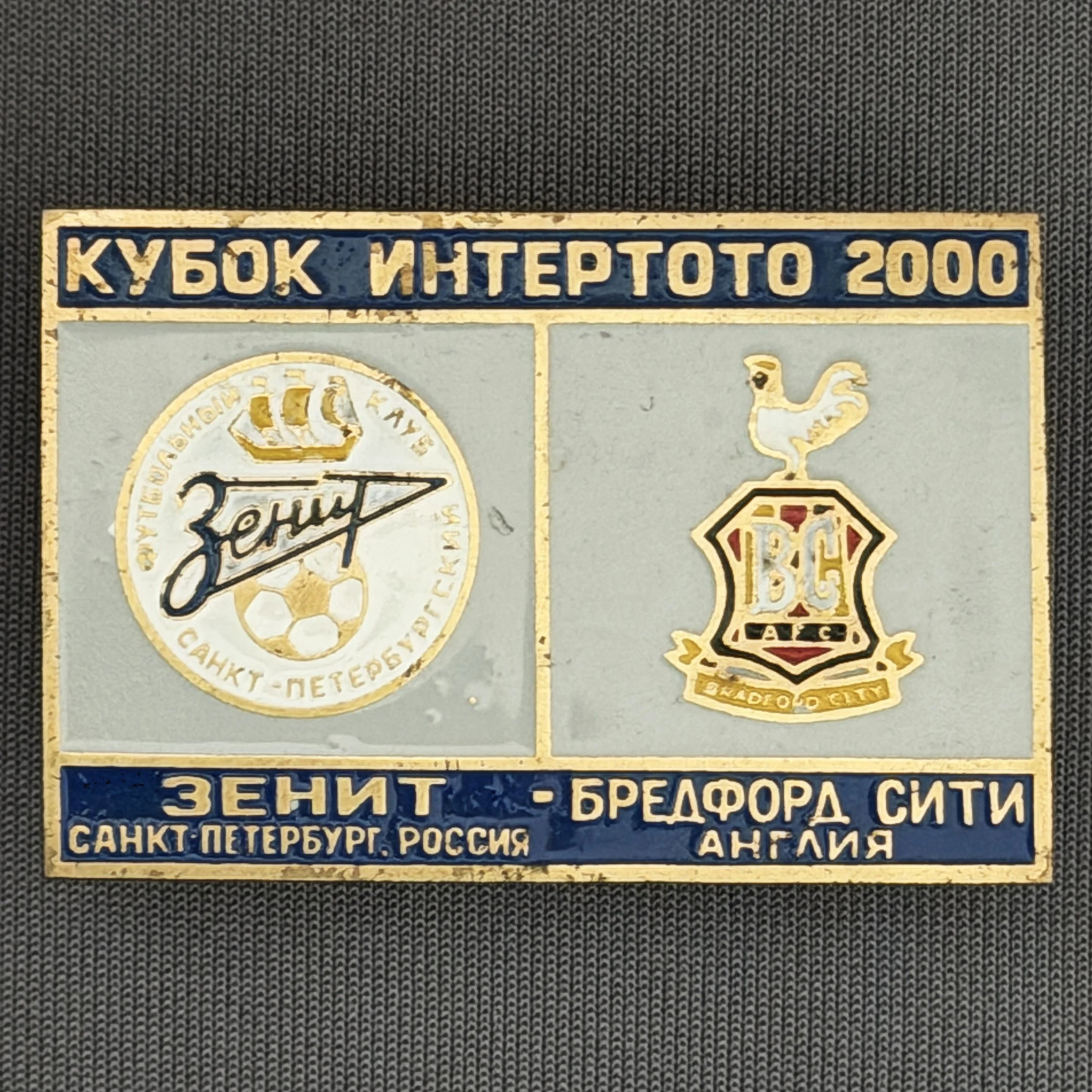 Reference Number: BCRUS045
Size: H 29.6 mm x W 44.6 mm
Pin Type: Metal Clutch
Plating: Antique Gold
Value: £12
Manufacturer: Unknown
Comments: Zenit St. Petersburg Inter Toto Cup, Dark Blue Top, Grey Middle, Dark Blue Bottom. Different Bantam.