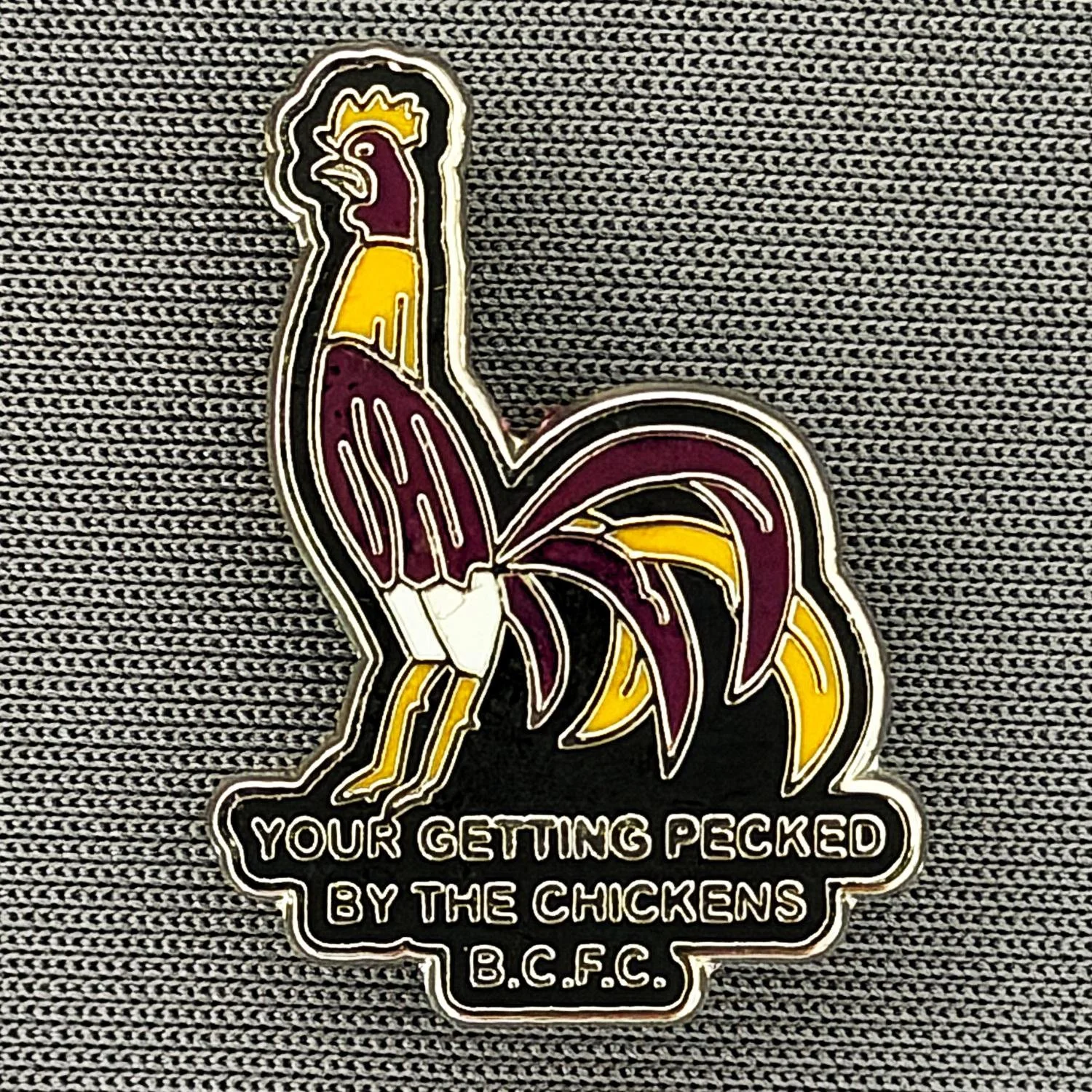 Reference Number: BCBAN063
Size: H 24.7 mm x W 17.9 mm
Pin Type: Brooch Pin
Plating: Silver
Value: £6
Manufacturer: Unknown
Comments: Claret & Amber & Black Bantam, Pecked By The Chickens 