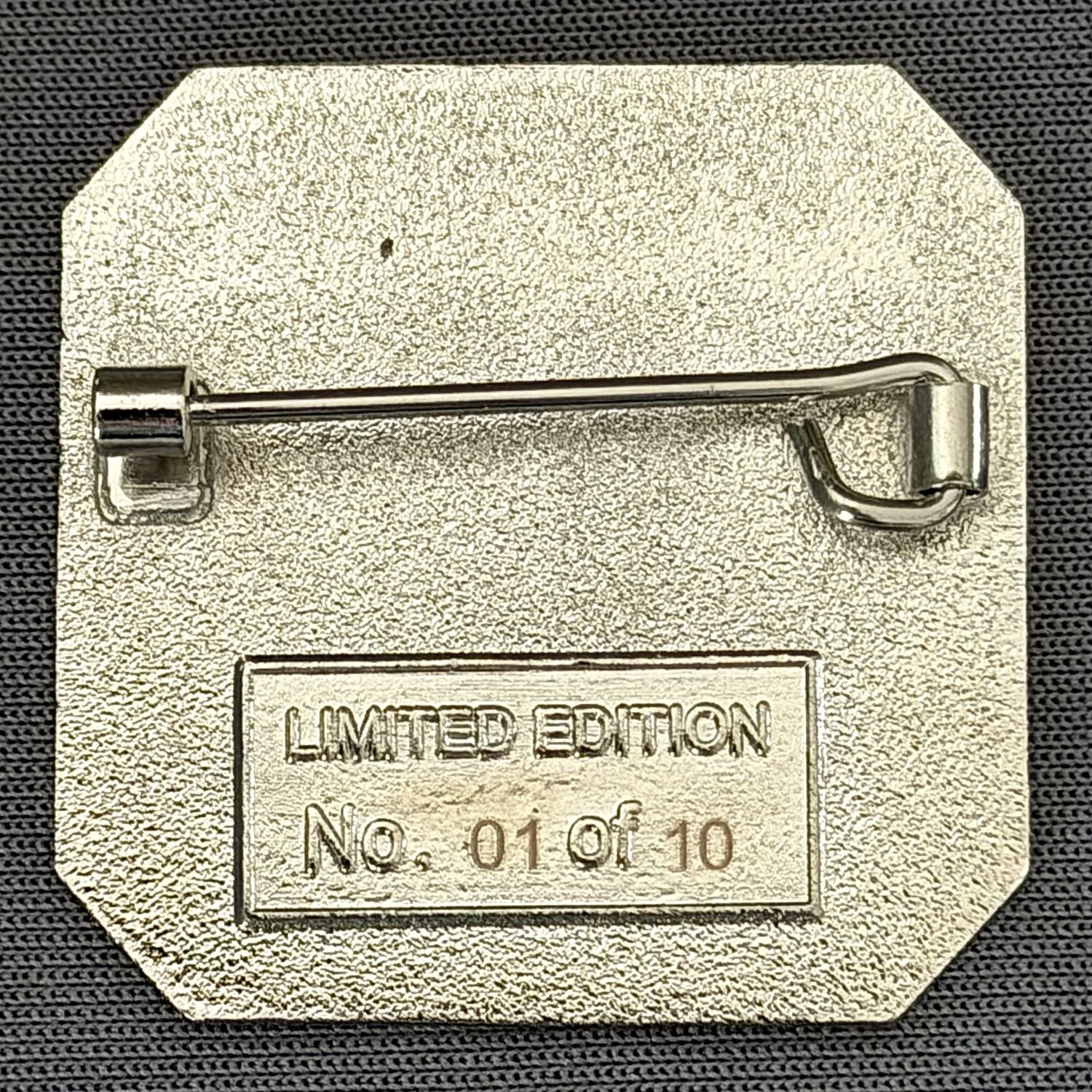 Silver badge with a pin at the top and embossed text reading "Limited Edition No. 01 of 10" on a black textured background.