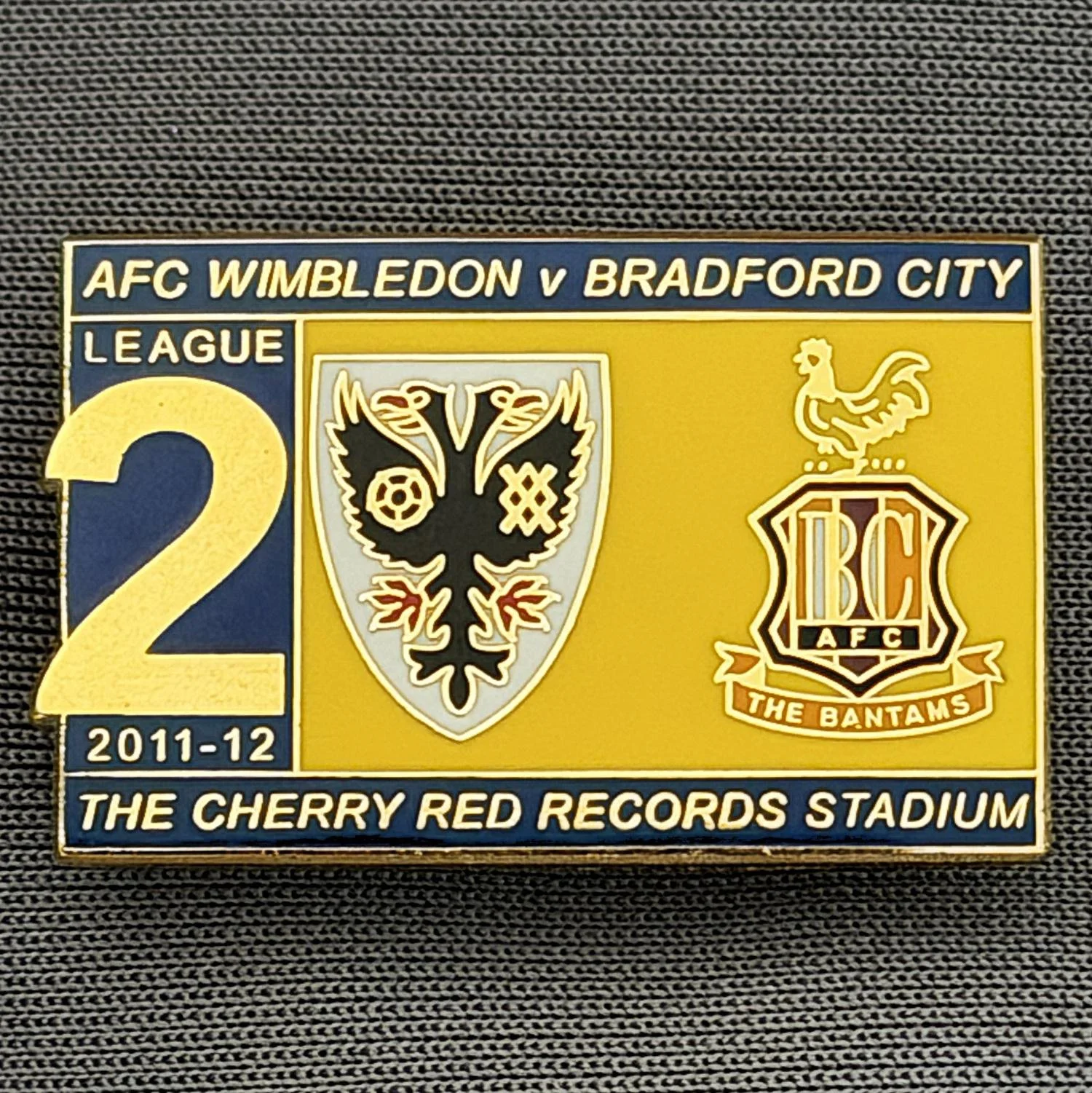 Reference Number: BCOFIX110
Size: H 18.1 mm x W 28.6 mm
Pin Type: Brooch Pin
Plating: Gold
Value: £5
Manufacturer: Terry's Badges
Comments: A.F.C. Wimbledon v Bradford City, League Two 2011/12 
