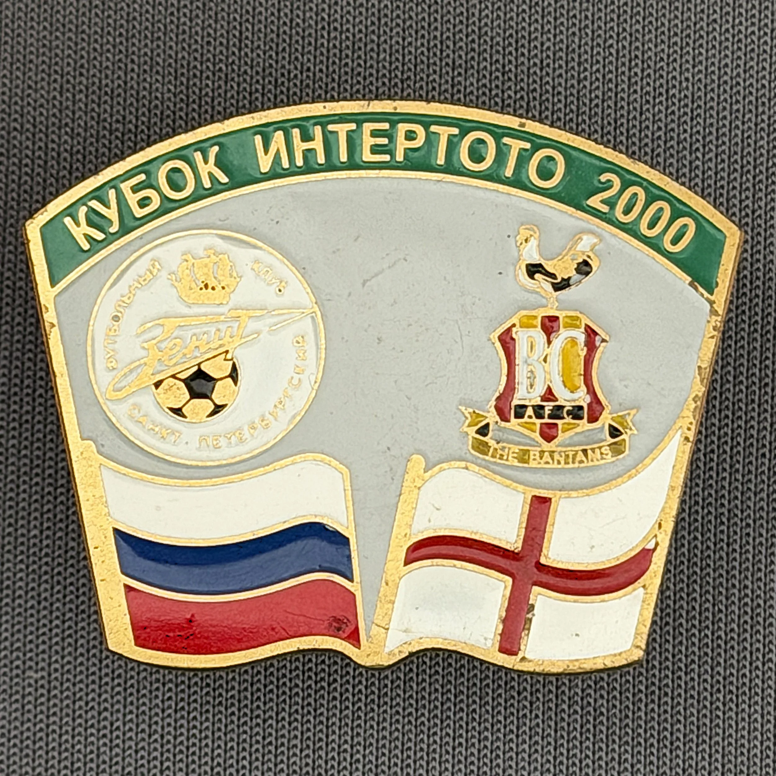 Reference Number: BCRUS034
Size: H 26 mm x W 32.3 mm
Pin Type: Metal Clutch
Plating: Antique Gold
Value: £12
Manufacturer: Unknown
Comments: Zenit St. Petersburg Inter Toto Cup, Green Top, Grey Background, Different Bantam